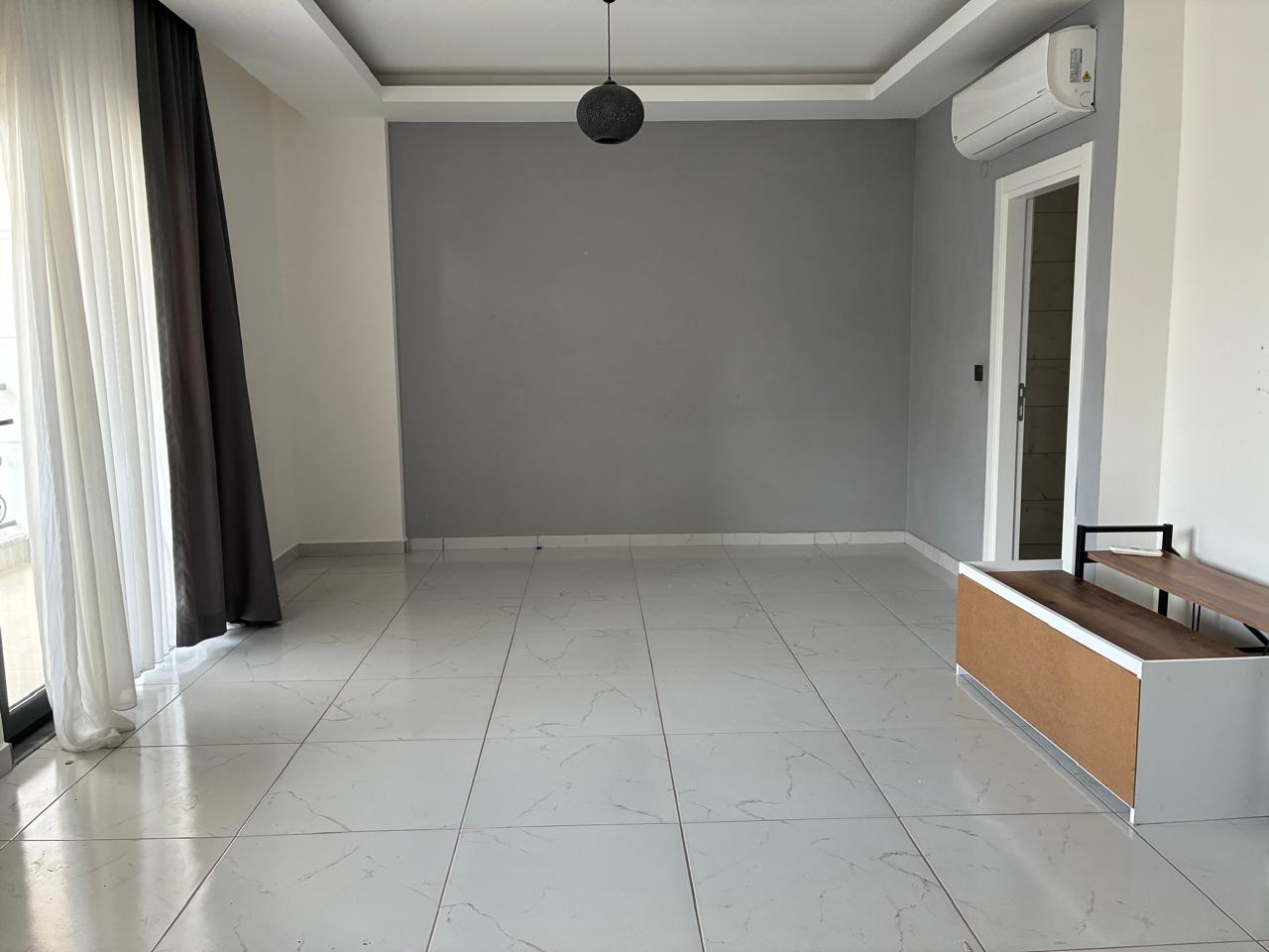 Living area with a white-and-wood TV unit and balcony door in a 2+1 penthouse for sale in Mahmutlar
