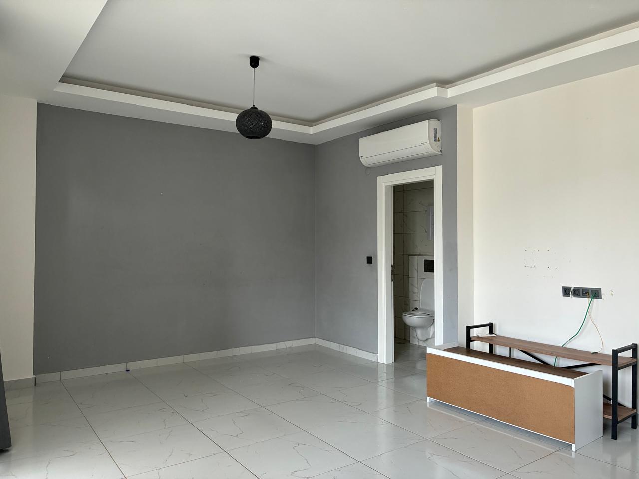 Empty living room with a grey accent wall and low TV unit in Turkey where the home is for sale