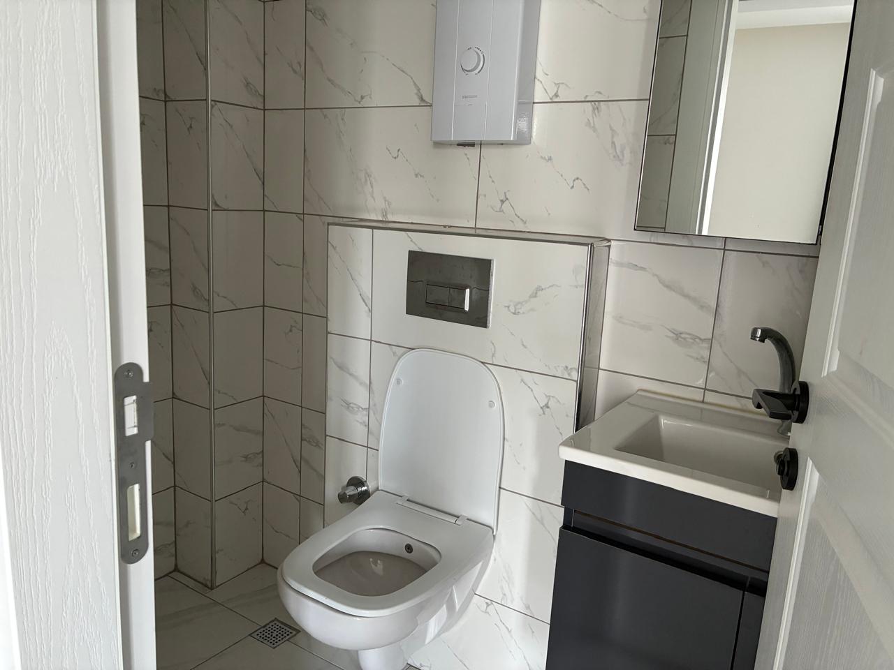 Bathroom with a black vanity, rectangular basin and marble-look wall tile in a duplex in Alanya