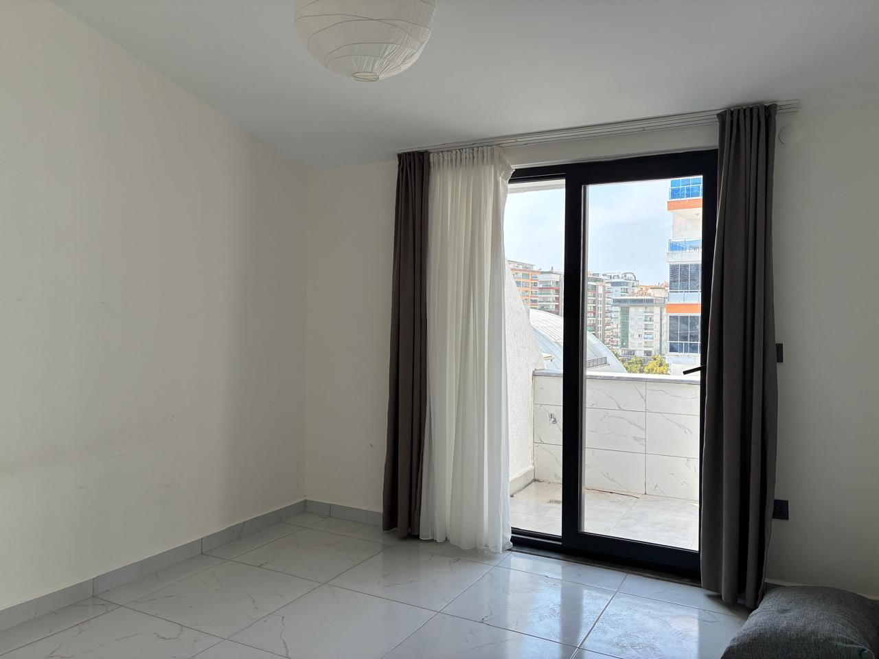 Empty bedroom with a sliding balcony door and neighbouring building views in a duplex in Alanya