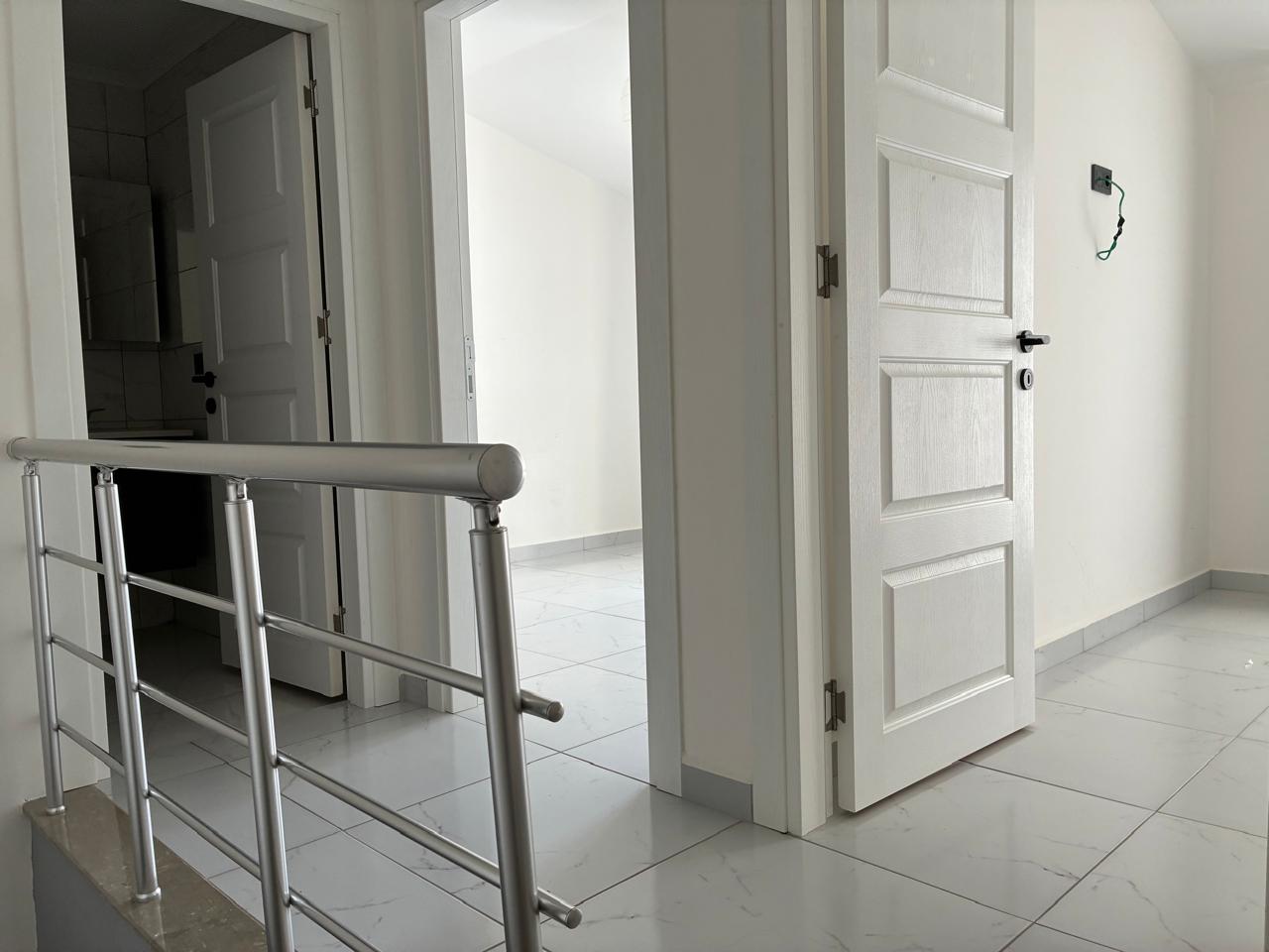 Hall with a metal stair railing, three white doors and light grey floor tiles in an apartment