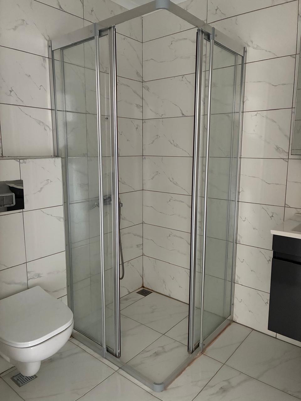 Bathroom with a corner glass shower, wall-hung toilet and chrome shower rail in a residence