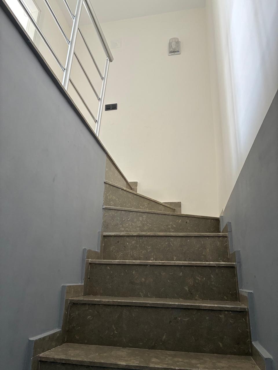 Staircase with grey stone steps, a turning flight and metal railings in a penthouse in Mahmutlar