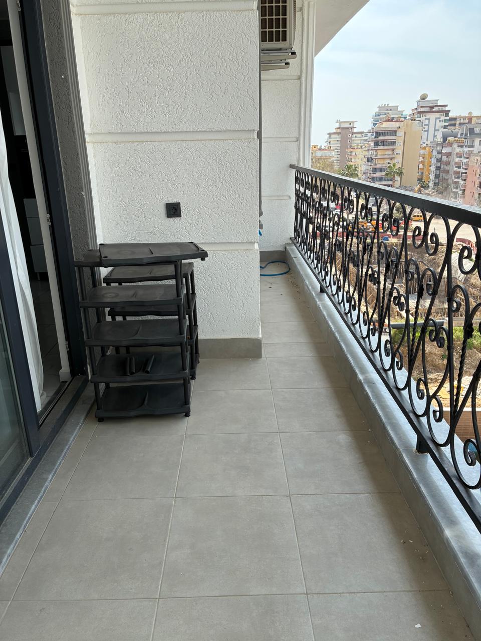 Narrow balcony with grey tiles, wrought-iron railing and city buildings in a duplex for sale in Alanya