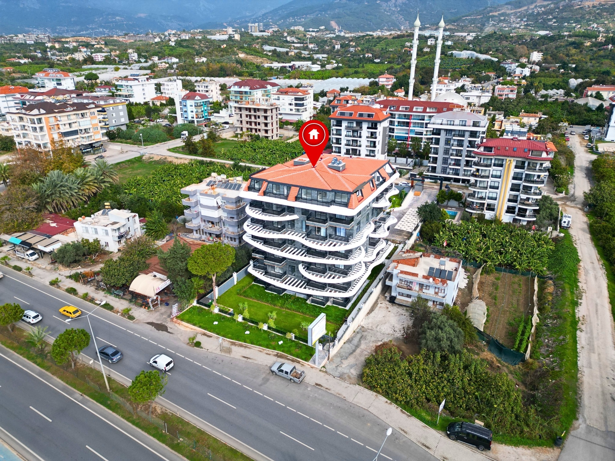 Dark stone facade with wave-shaped balconies and a lawn at a residence in Alanya, Turkey