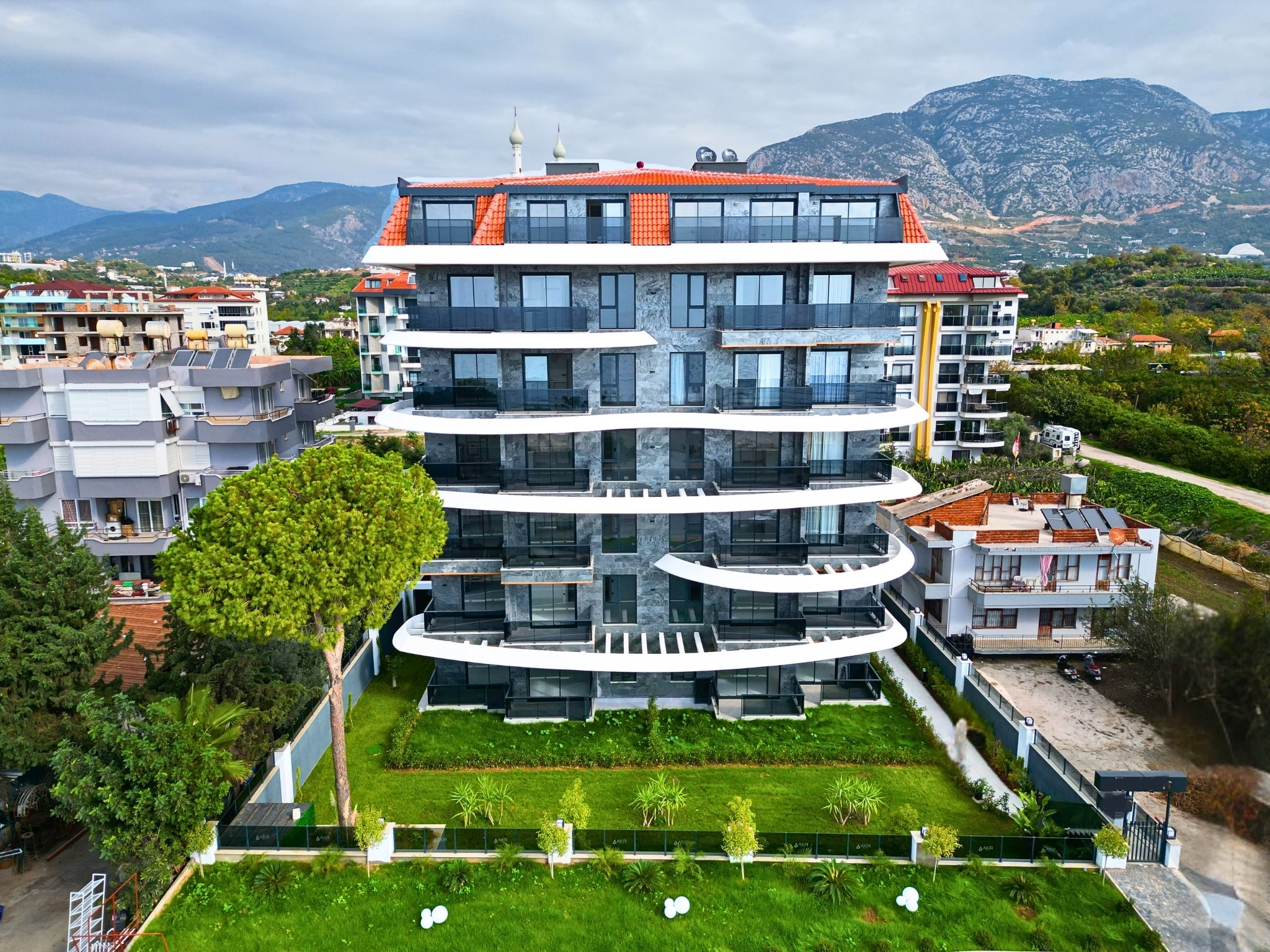 Stone-clad facade of a residence for sale in Turkey with rounded white balconies and a conifer tree