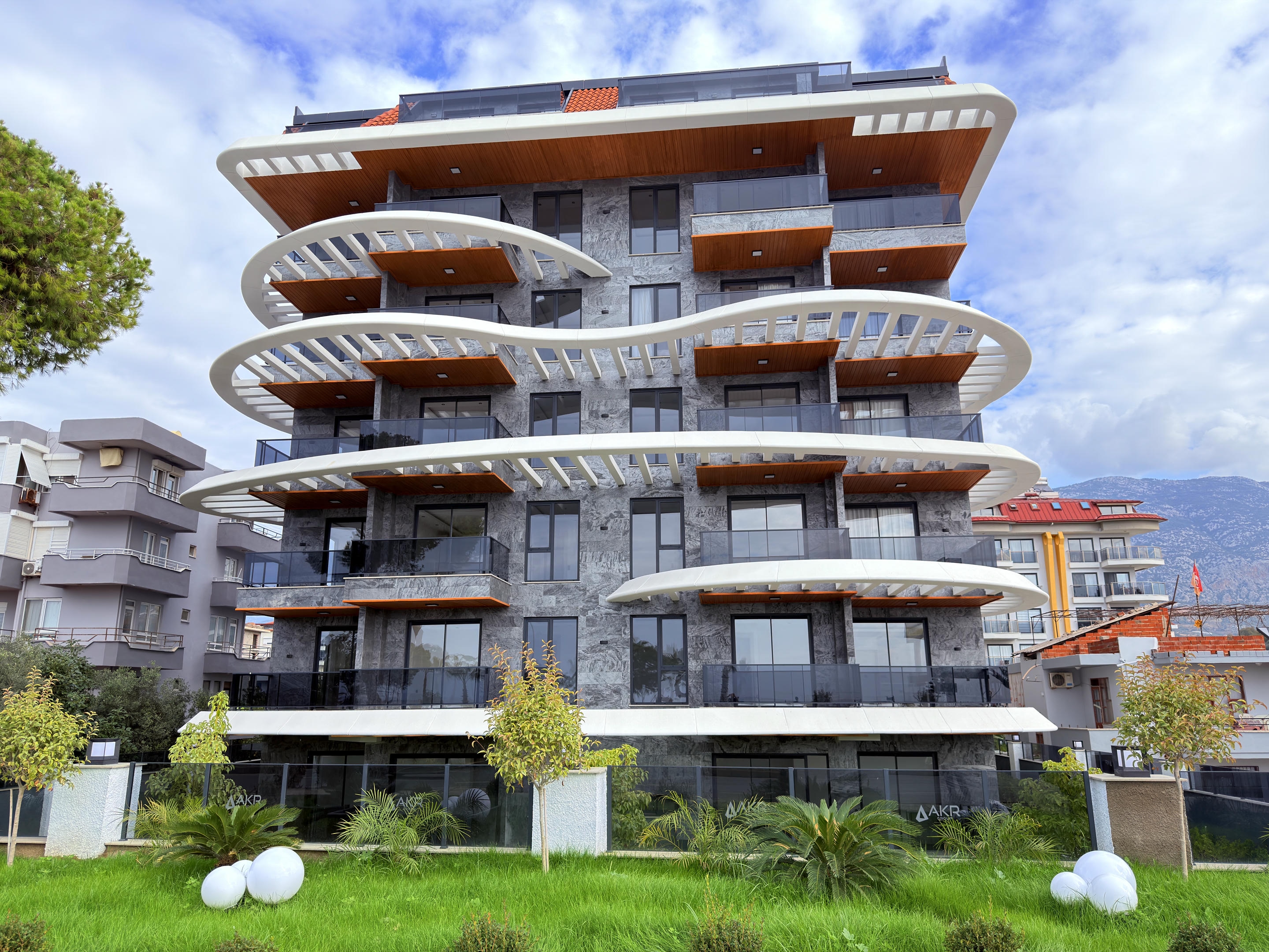 Gray stone facade with wooden balcony soffits and rounded white balconies at a duplex in Türkiye