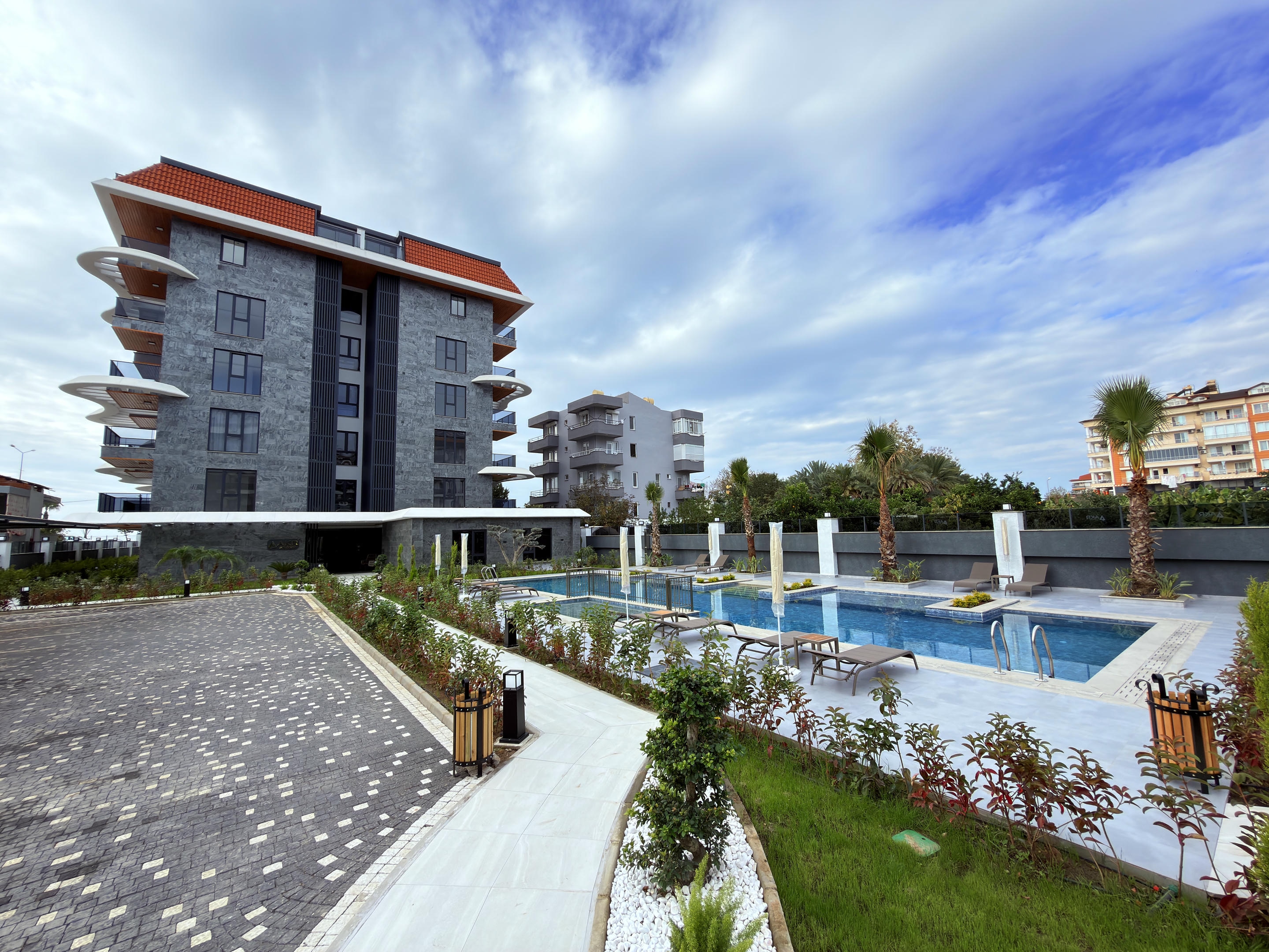Blue-tiled outdoor pool with brown loungers and palm beds near the sea