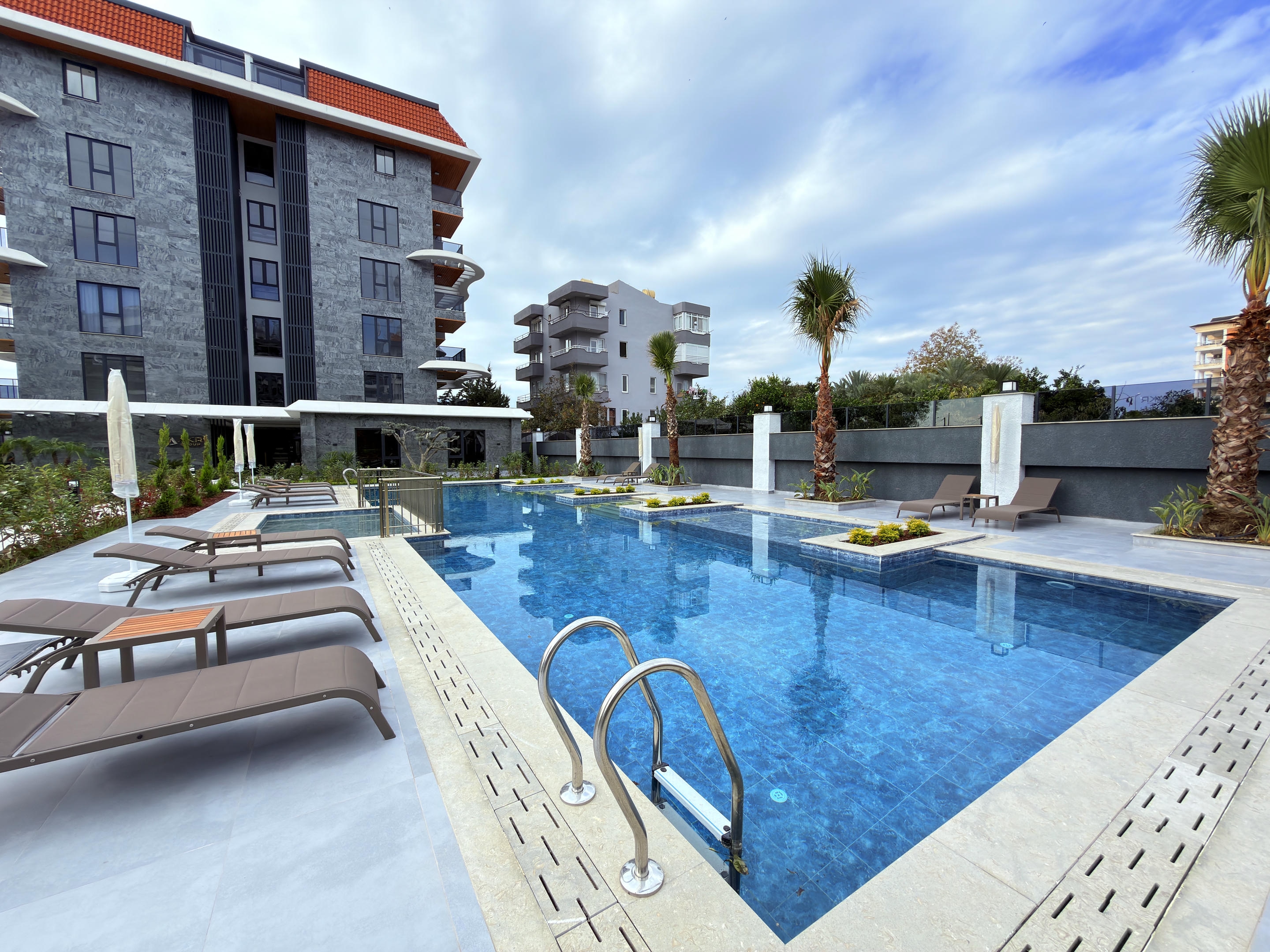 Mosaic-tiled outdoor pool with a metal ladder and loungers in a complex with apartments