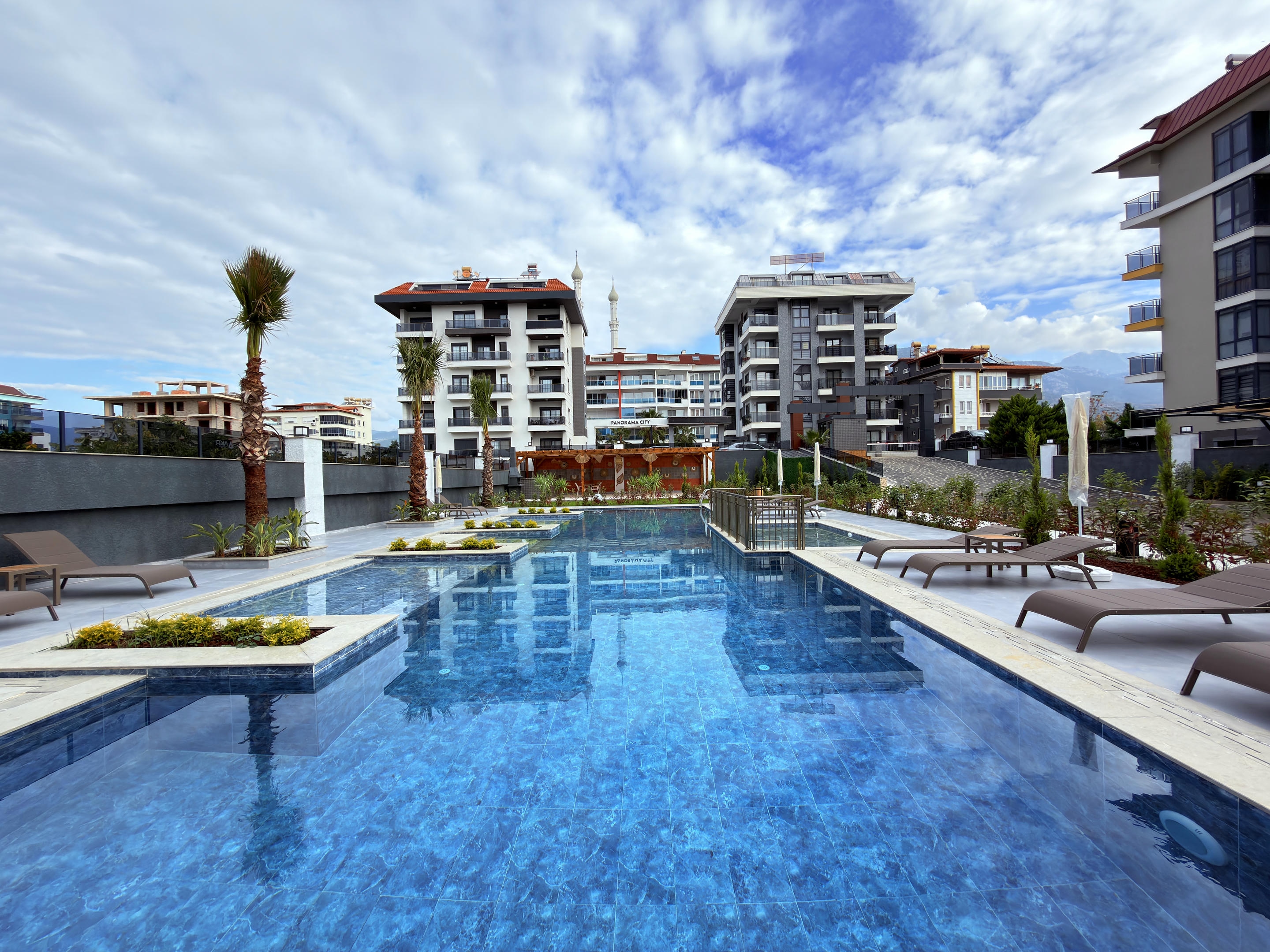 Large blue-tiled pool with planted beds in a complex where apartments are for sale in Turkey