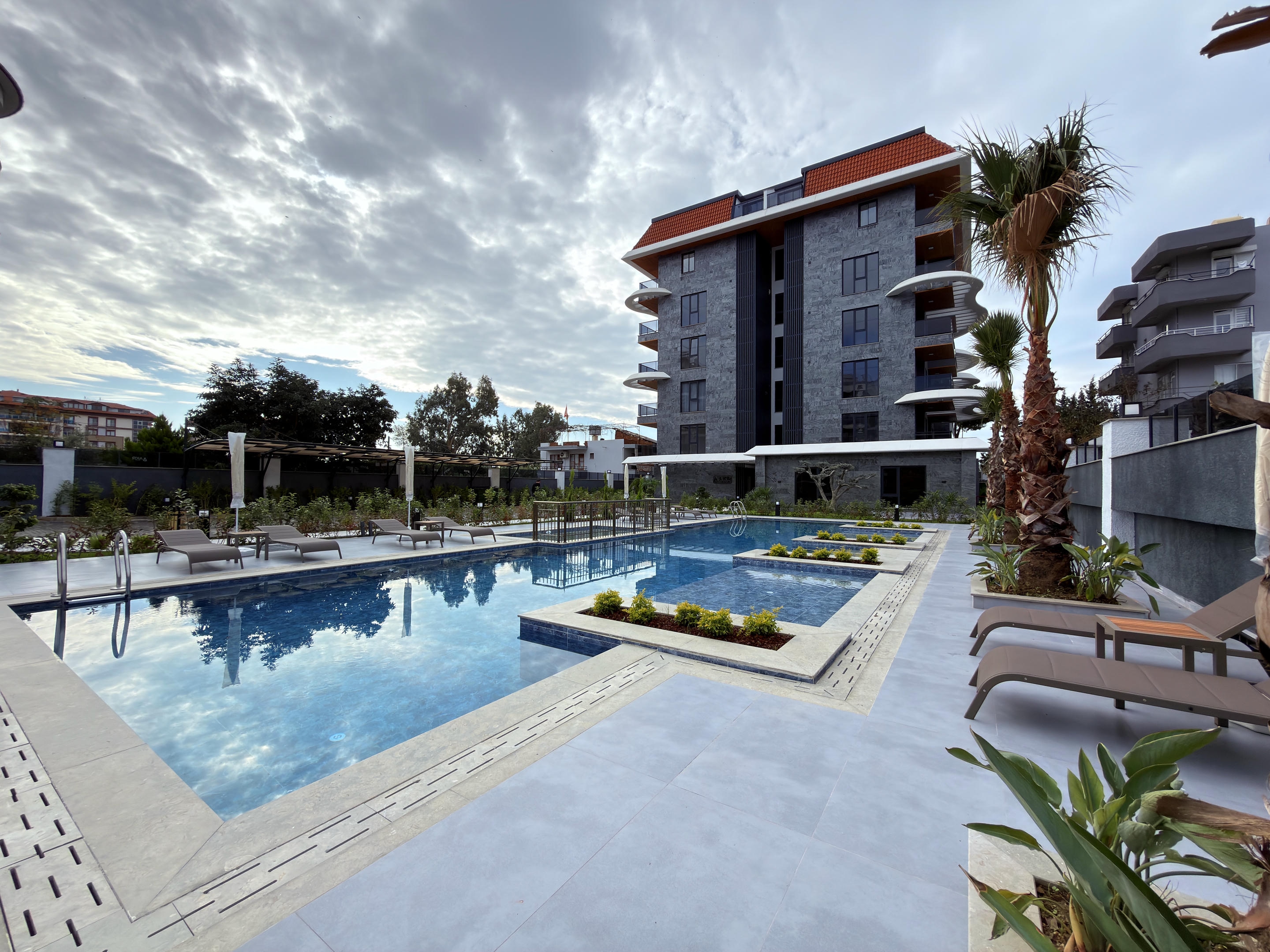 Evening outdoor pool with blue water, loungers and planted beds where apartments are for sale