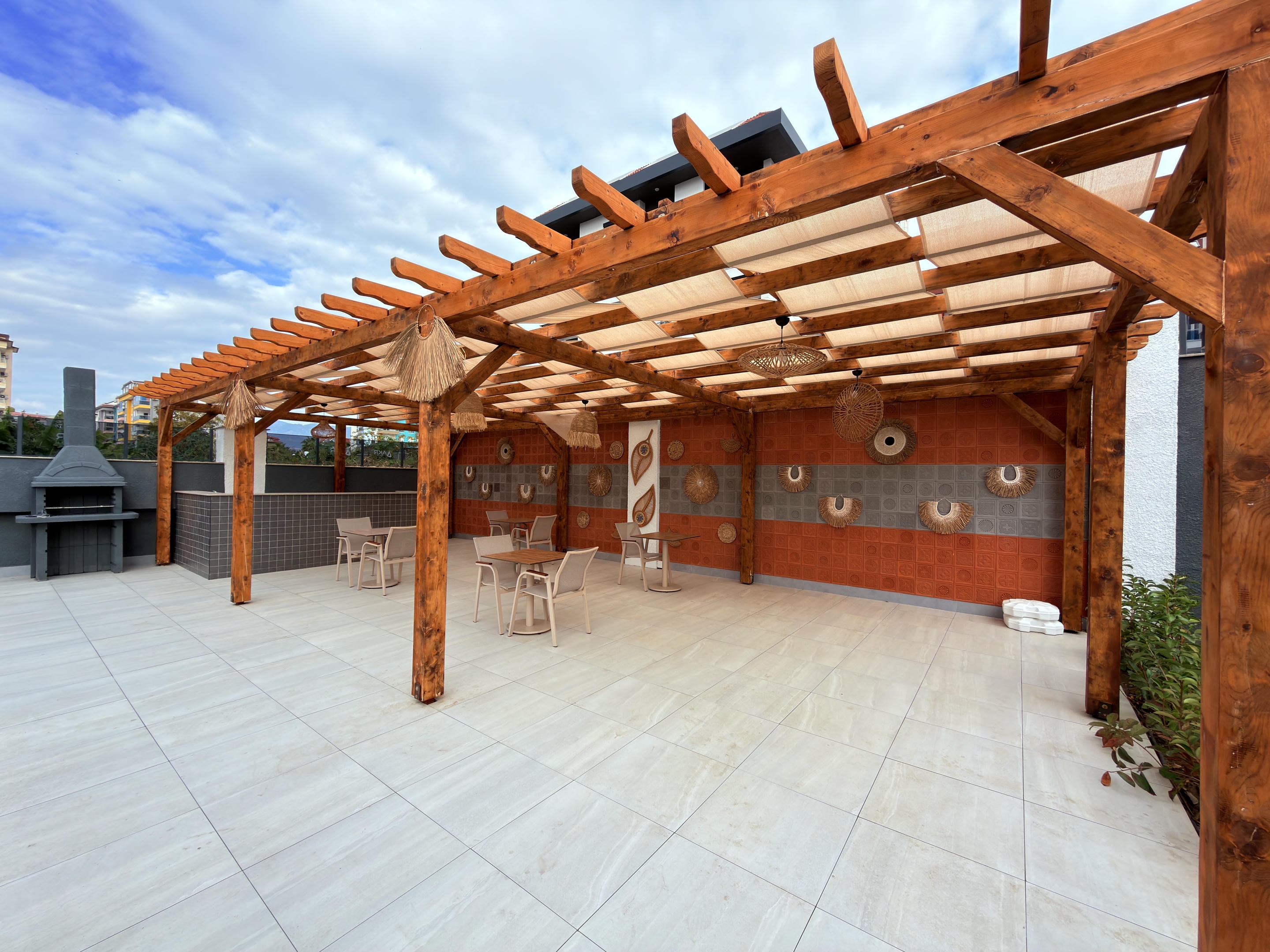 Wooden pergola at a complex where duplexes are for sale, with a fabric canopy and stone barbecue