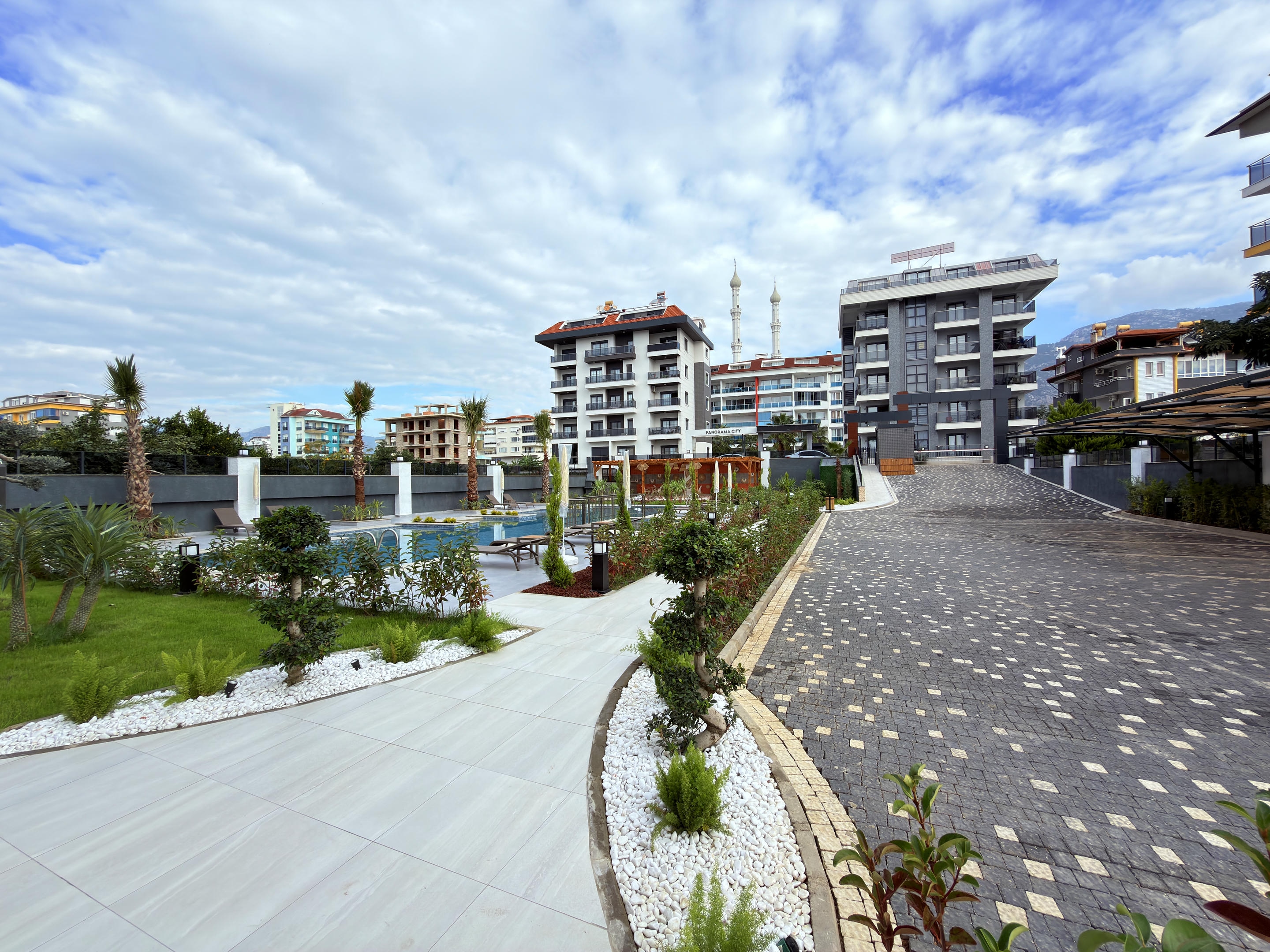 Curved tiled path leading to the pool with palms at a complex with apartments in Alanya
