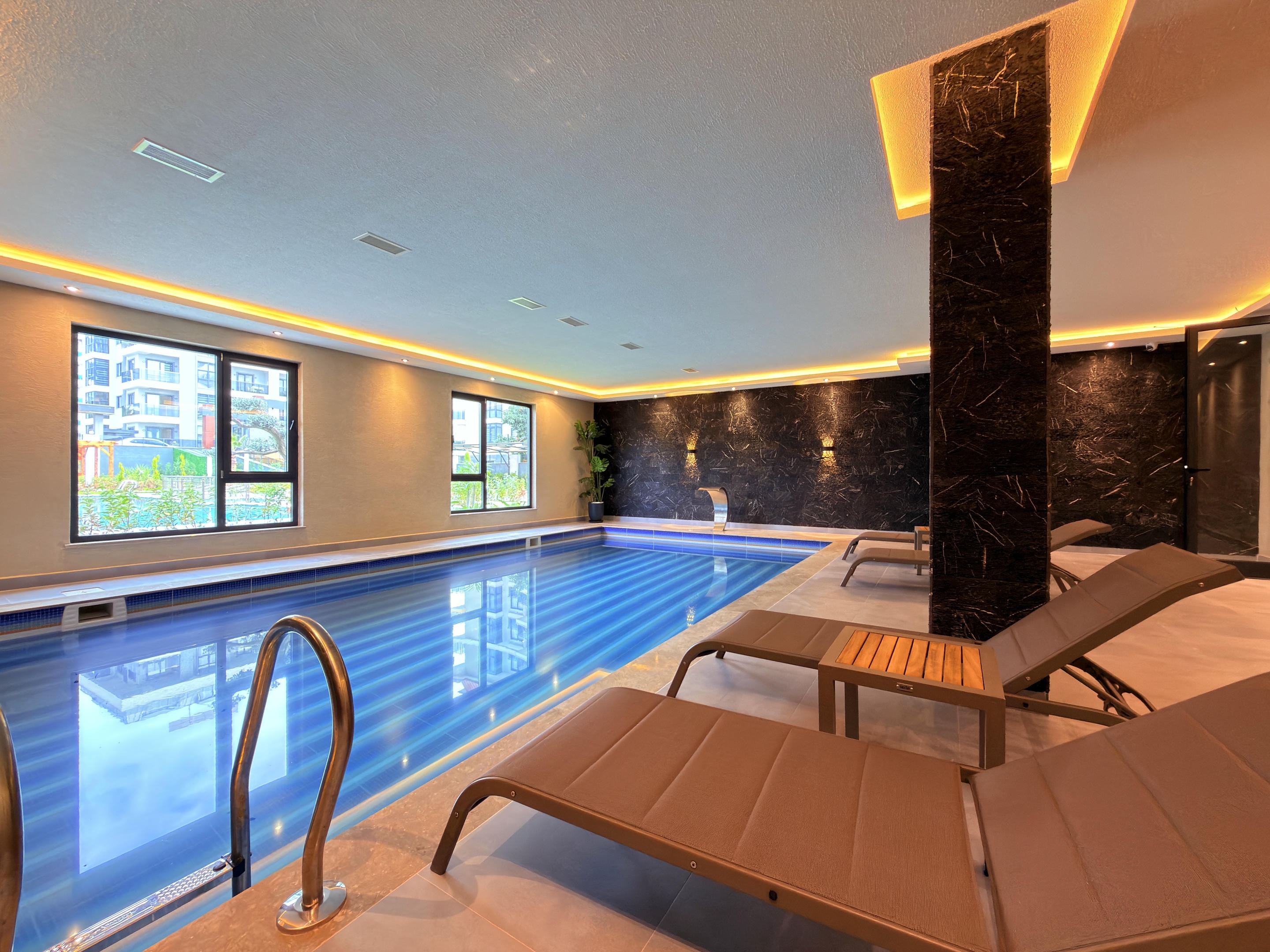 Indoor pool with black marble columns, gray loungers and windows facing the courtyard near the sea
