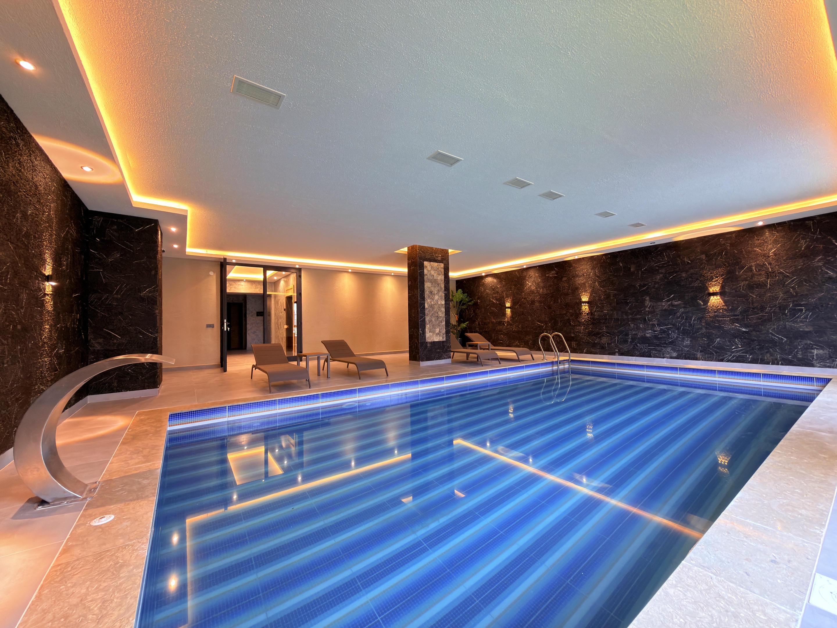 Indoor pool with blue mosaic tiles and a curved waterfall in a complex with apartments for sale in Turkey