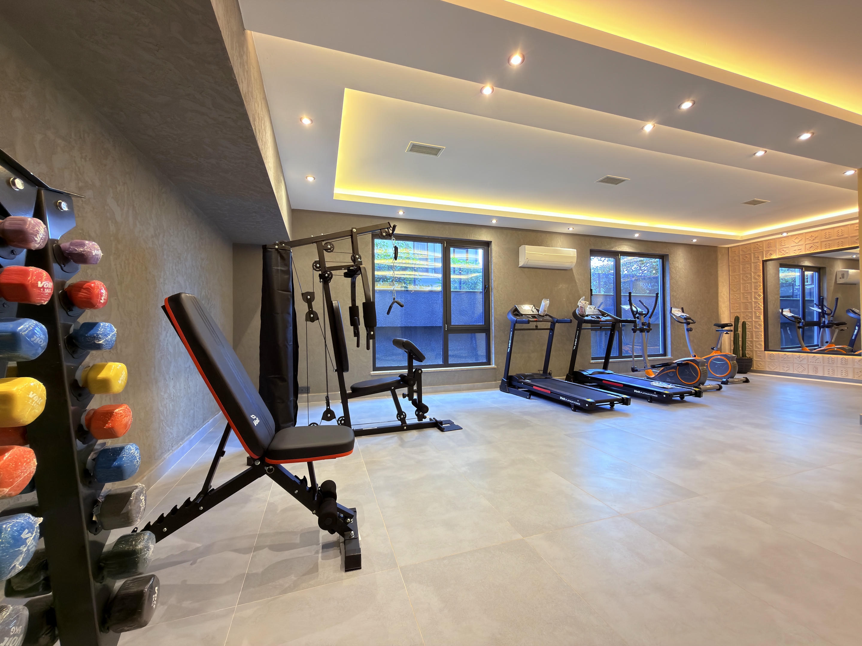 Gym with colorful dumbbells, a treadmill and panoramic windows for penthouse residents in Kestel