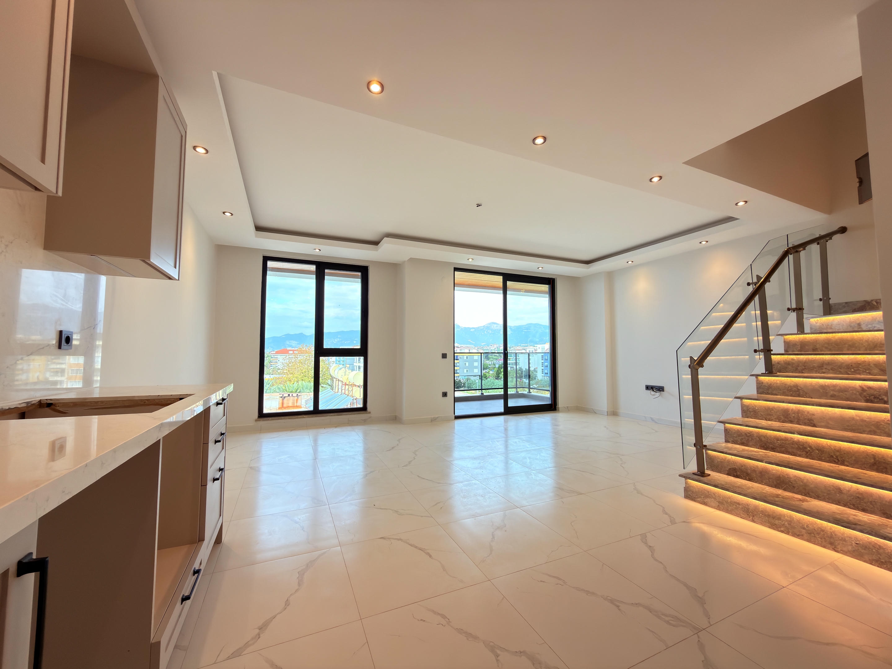 Kitchen-living room with a linear kitchen and warmly lit staircase in Kestel