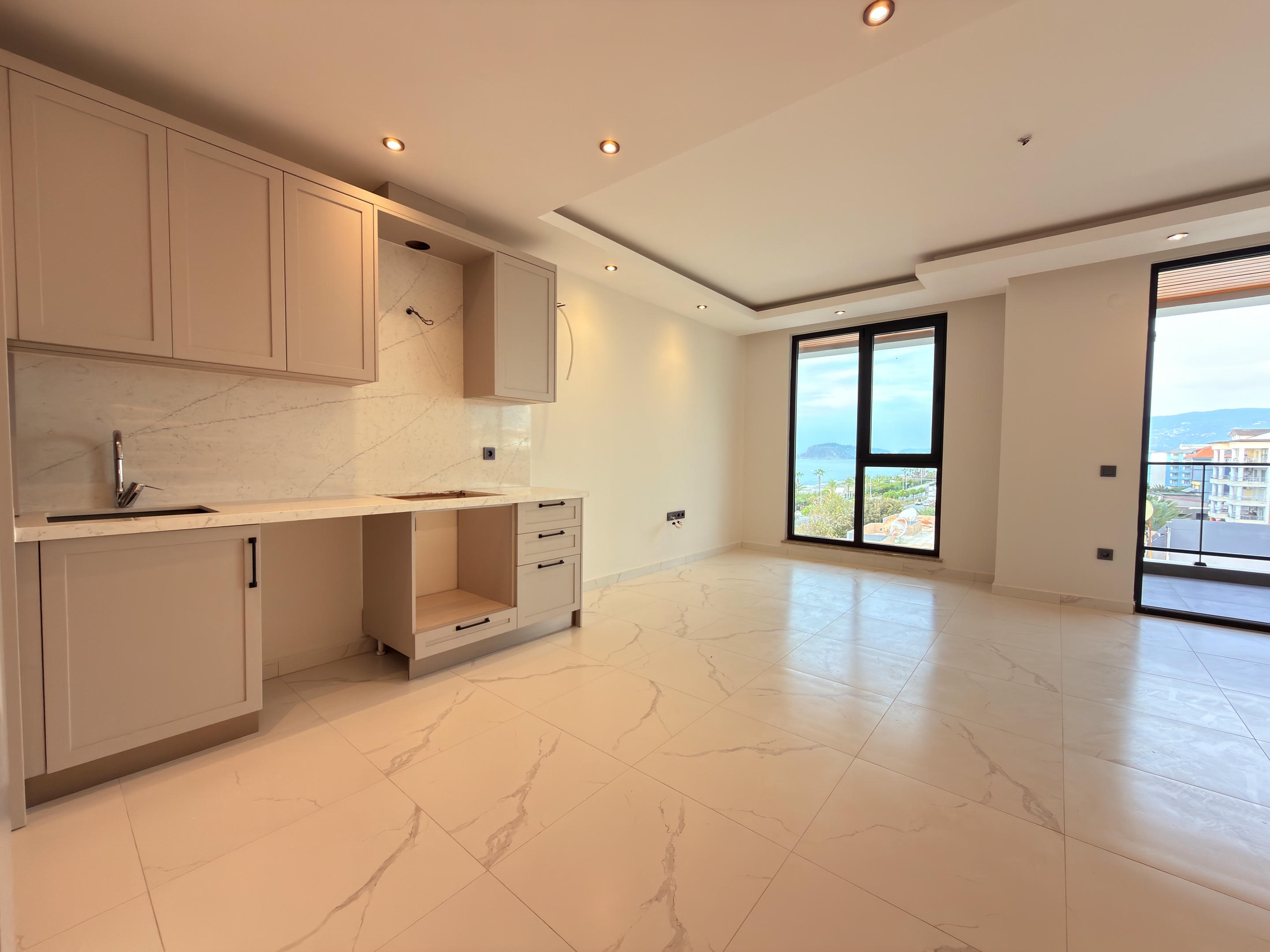 Kitchen-living room with light cabinets, marble-look backsplash and balcony door at a penthouse