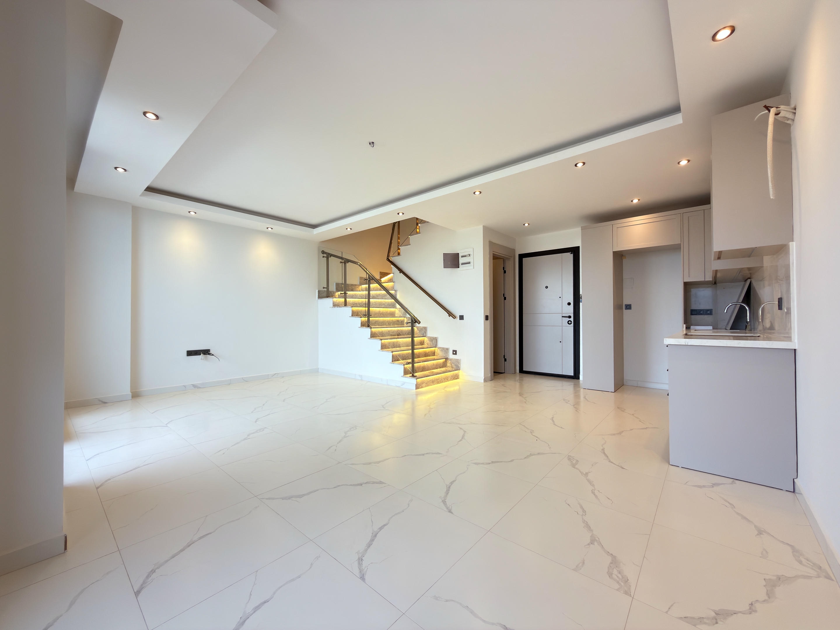 Open kitchen-living room with a corner kitchen and illuminated staircase at a residence in Kestel