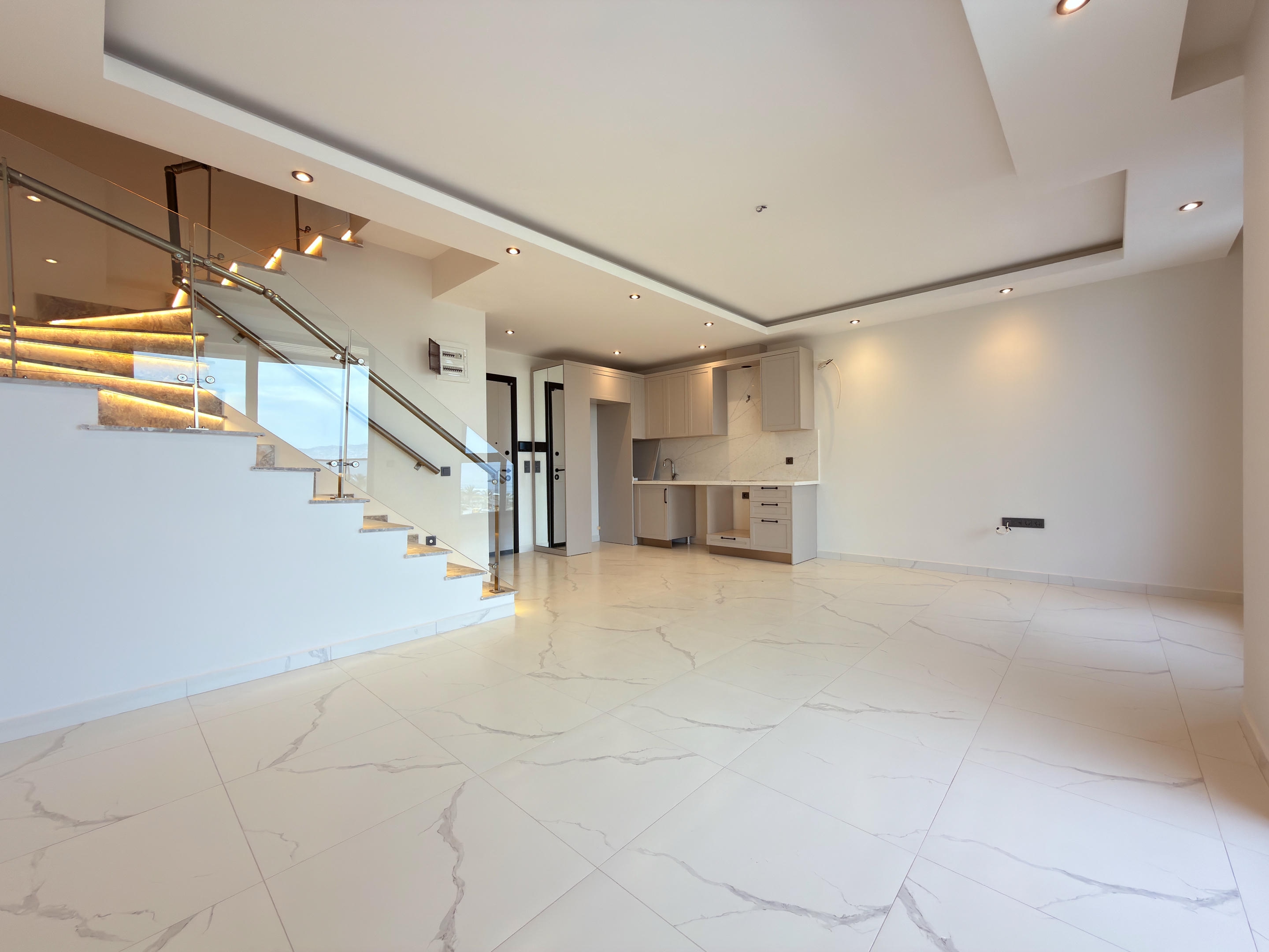 Empty kitchen-living room with a light kitchen line and glass stair railing at a duplex in Turkey