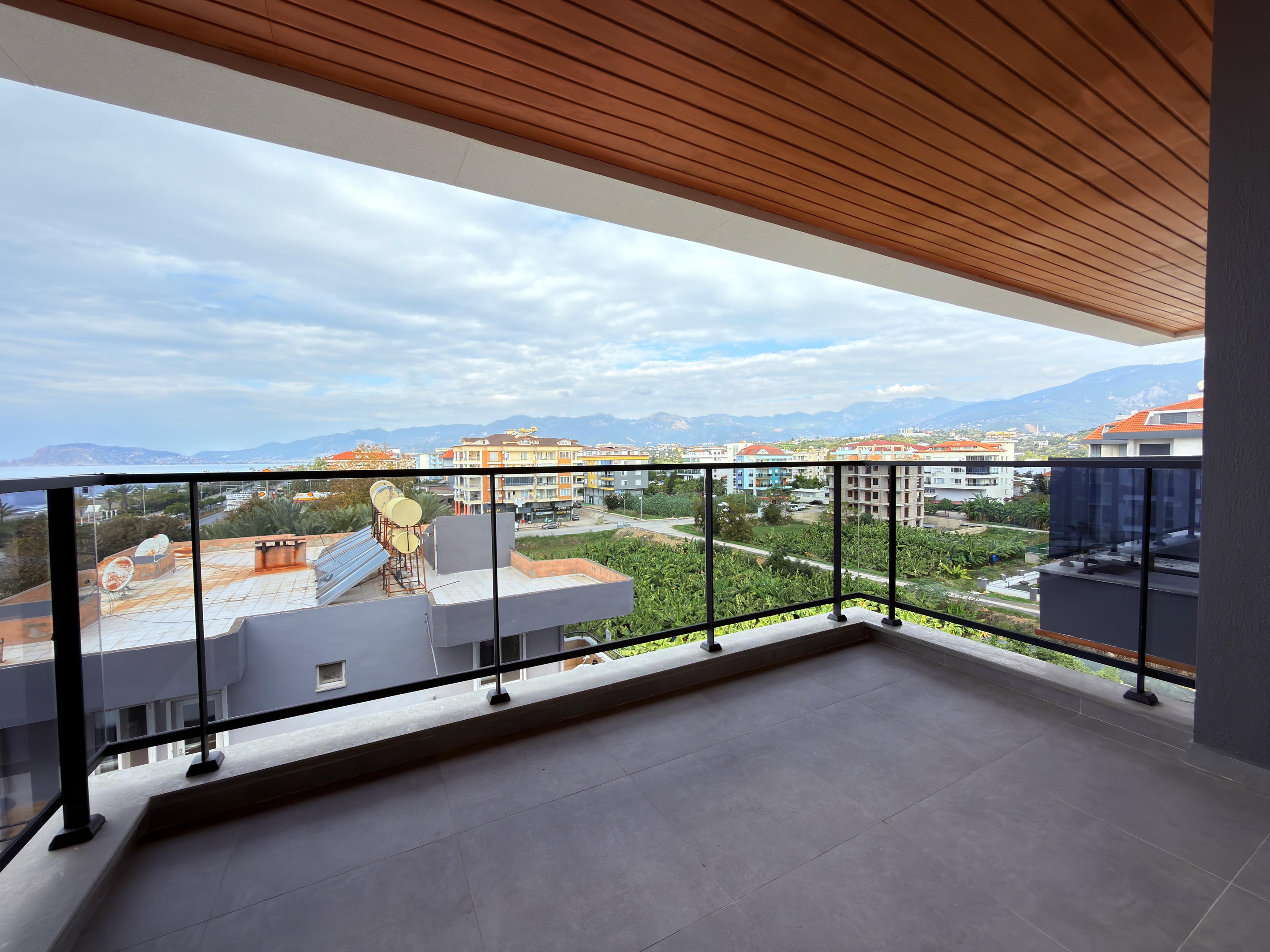 Corner balcony with glass railing overlooking residential buildings and distant mountains in Alanya