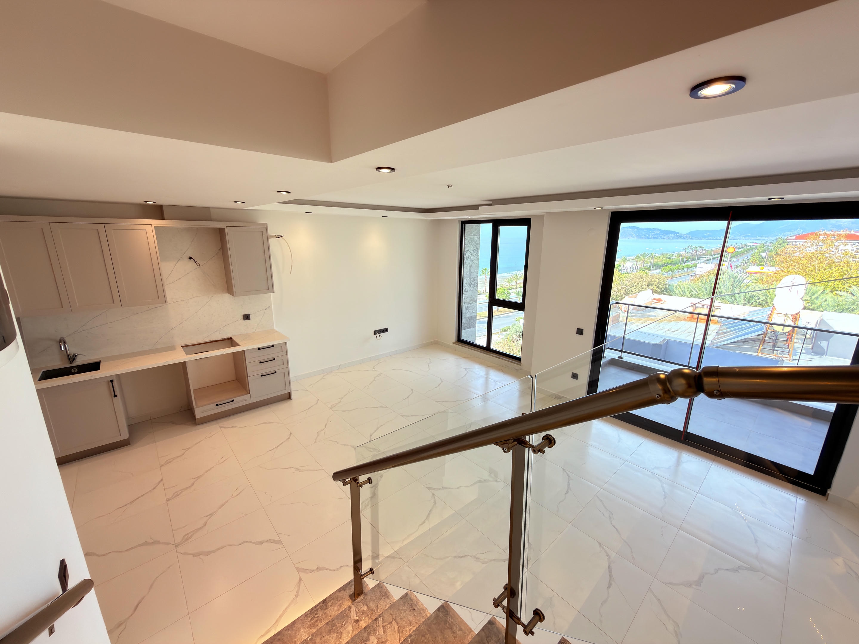 Kitchen-living room with glass-railed staircase and sea view through panoramic doors at a duplex in Kestel