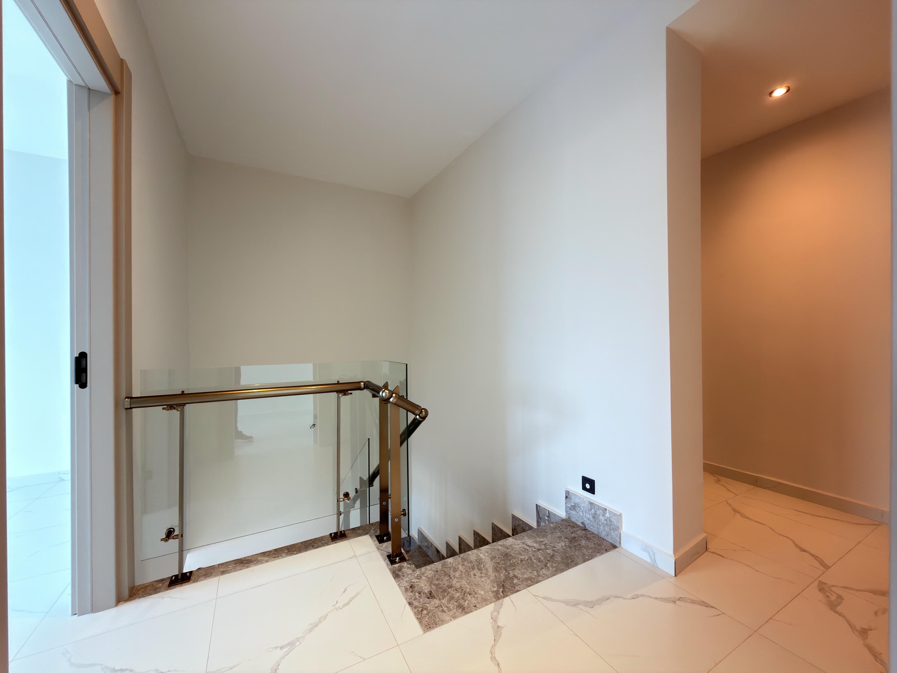 Interfloor staircase with gray stone steps, glass railing and bronze-toned handrails in a penthouse