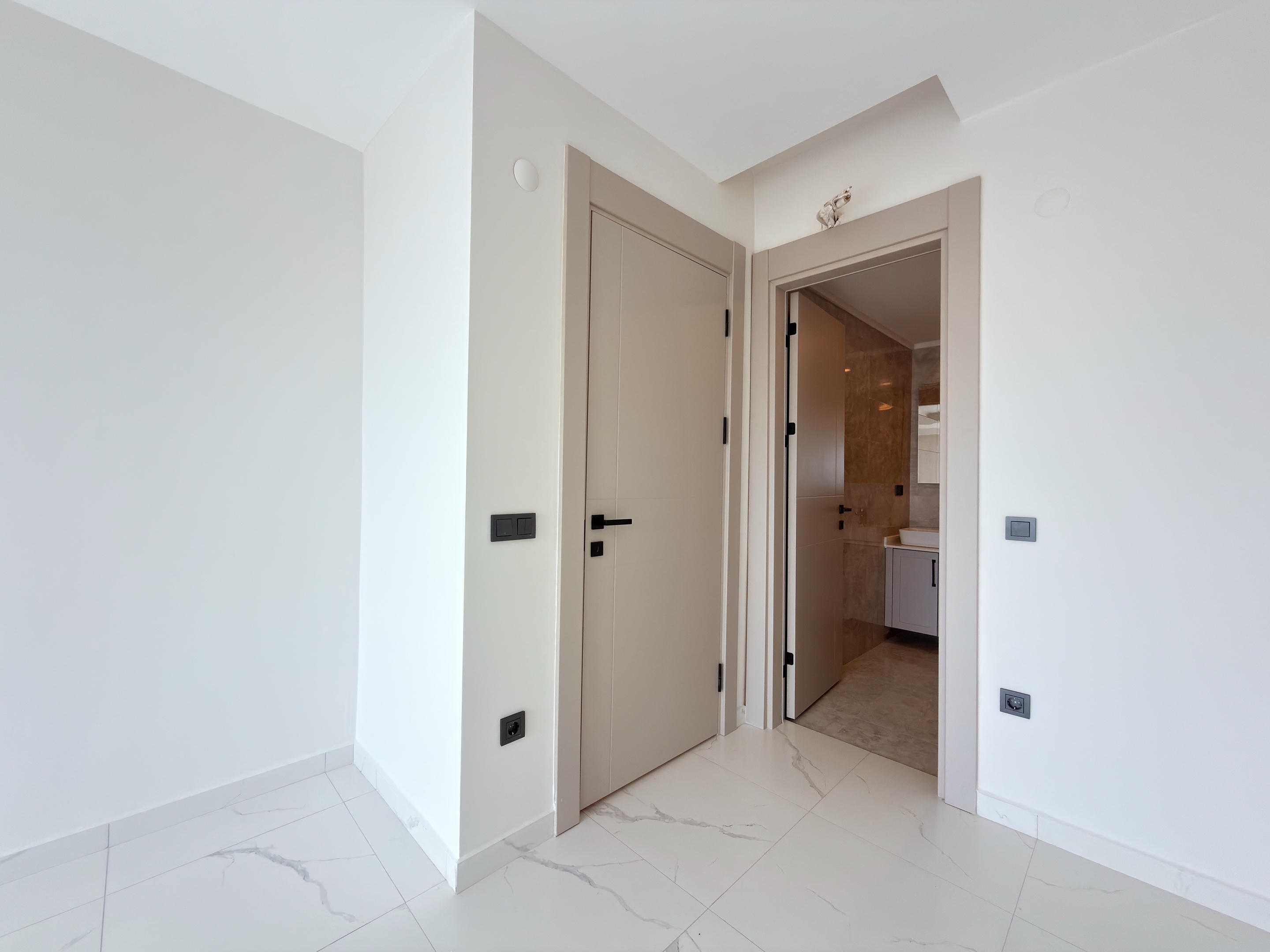 Bright bedroom with a bathroom door and marble-look porcelain floor in apartments in Alanya