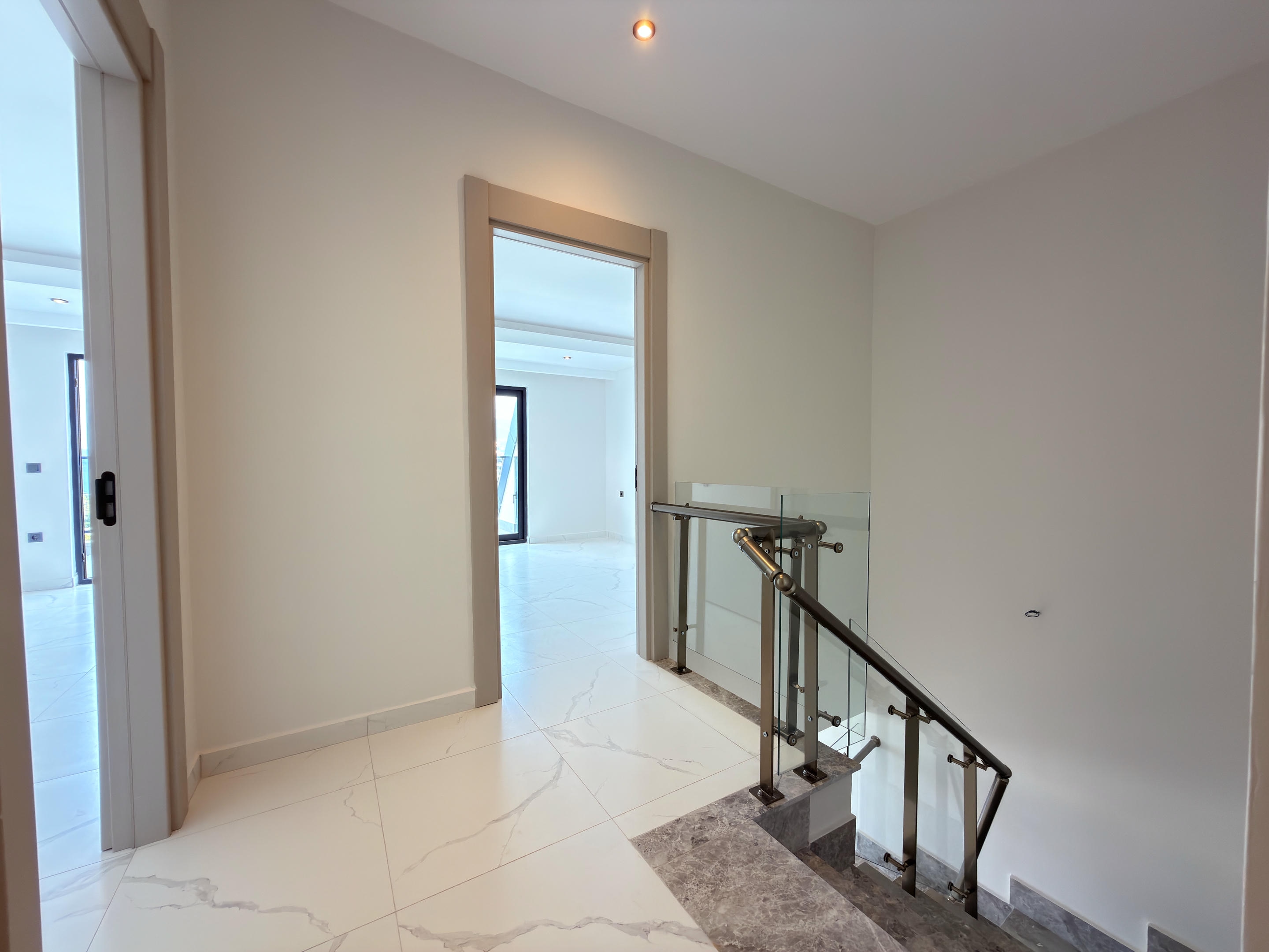 Interfloor staircase with glass railing and bronze-toned handrails at a duplex in Kestel