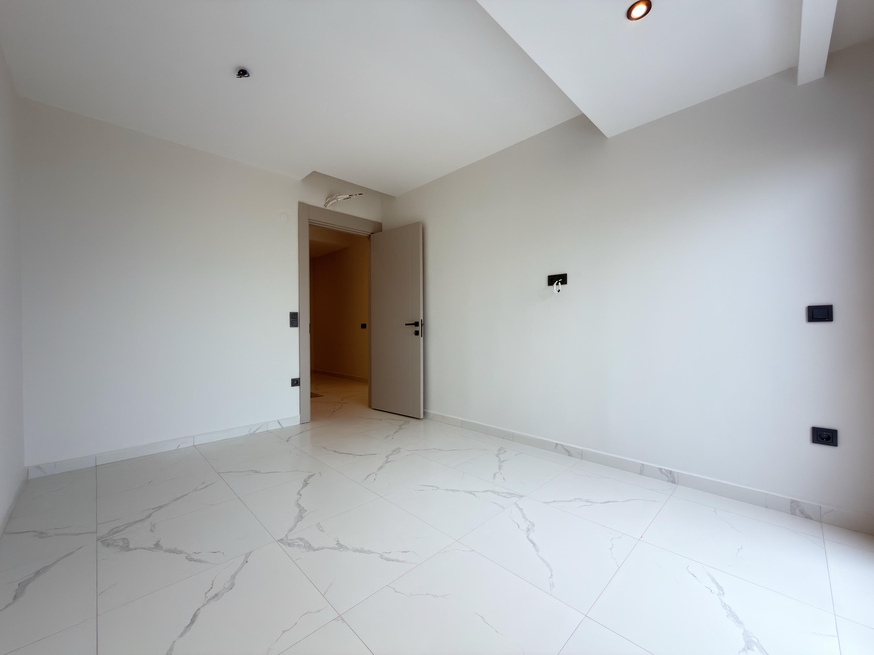 Bright empty room with a sloped white ceiling and marble-look floor tiles at a residence