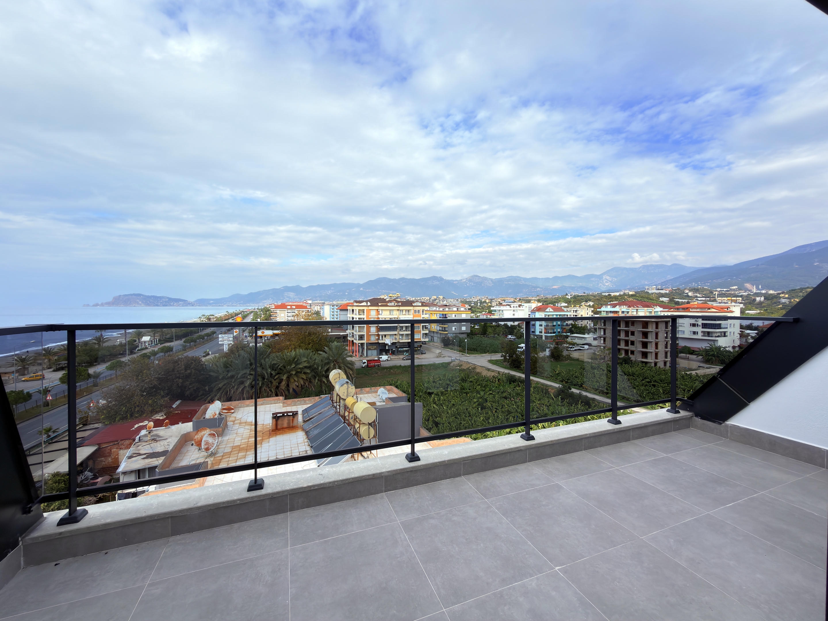 Spacious balcony with glass railing, panoramic sea view and distant mountain ridge at a penthouse in Alanya