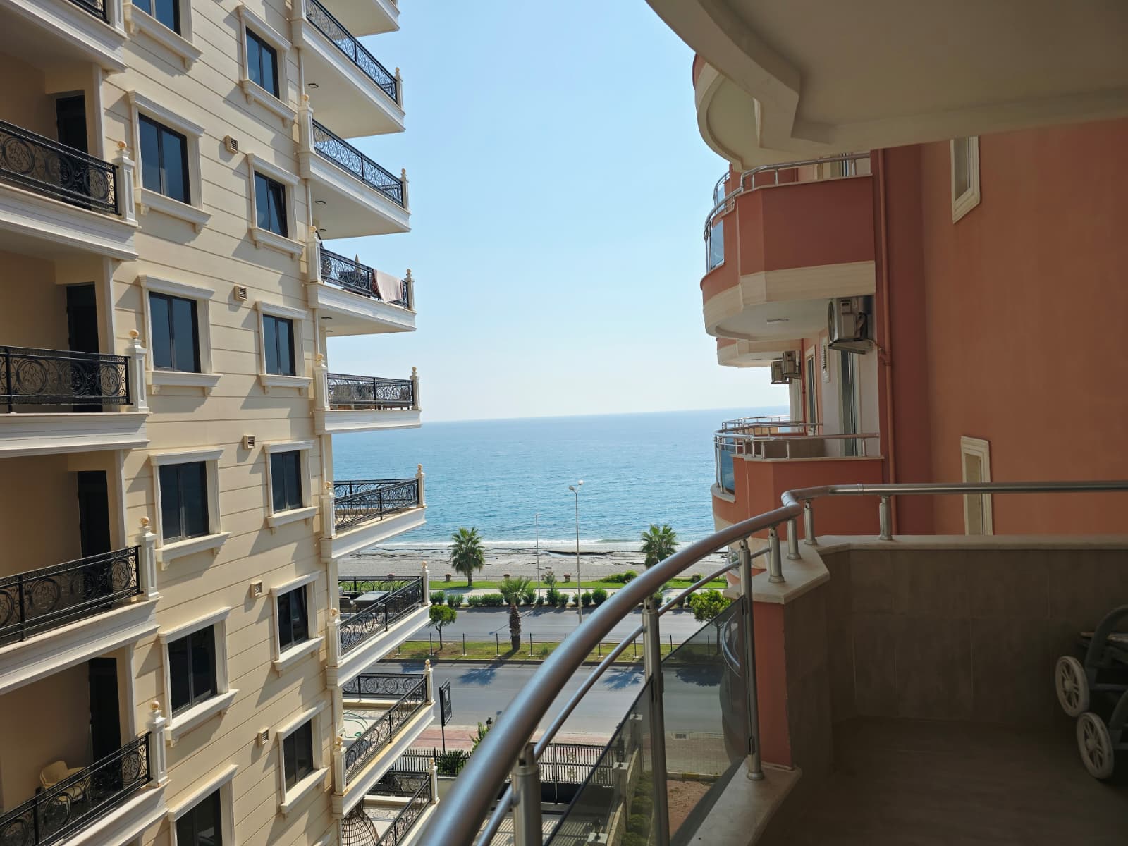 Вид с изогнутого балкона на море между домами и пальмы у апартаментов в Турции