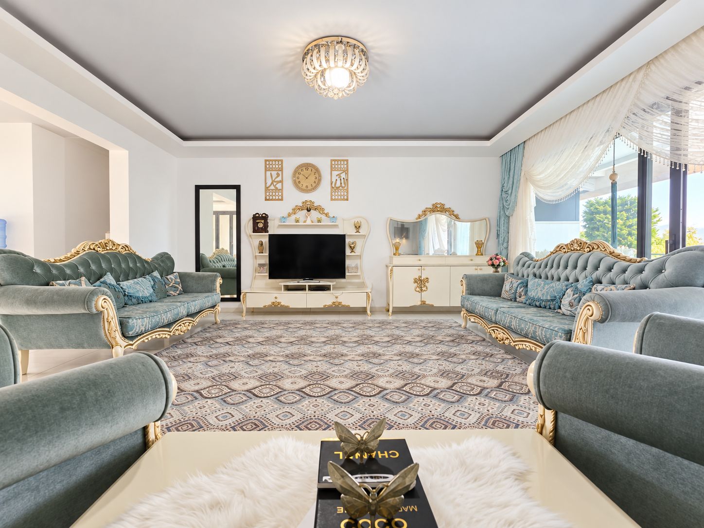 Two blue sofas with carved gold trim beneath a crystal chandelier in a duplex for sale in Türkiye