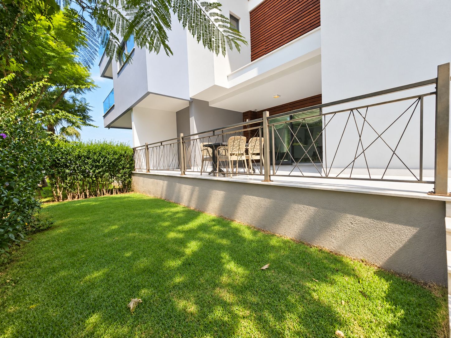 White residential facade with a terrace, lawn and wood slat cladding at a duplex in Kargicak