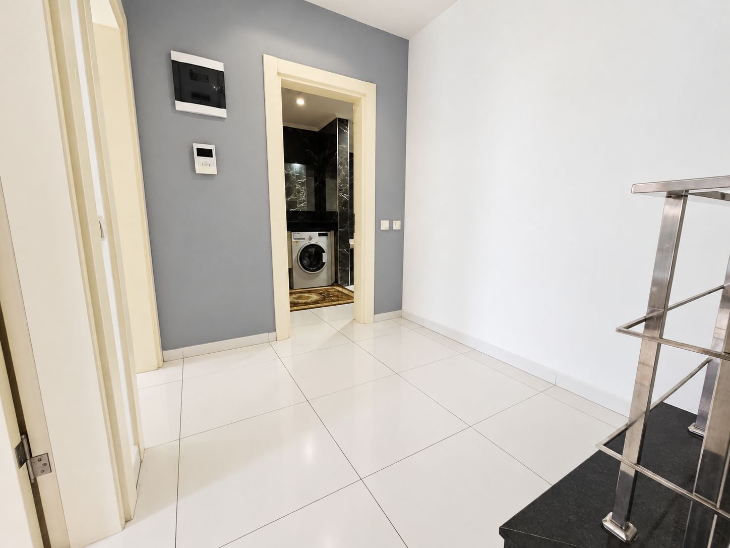 Corridor with dark stair treads, steel railing and an open doorway to the bathroom in a 2+1 apartment