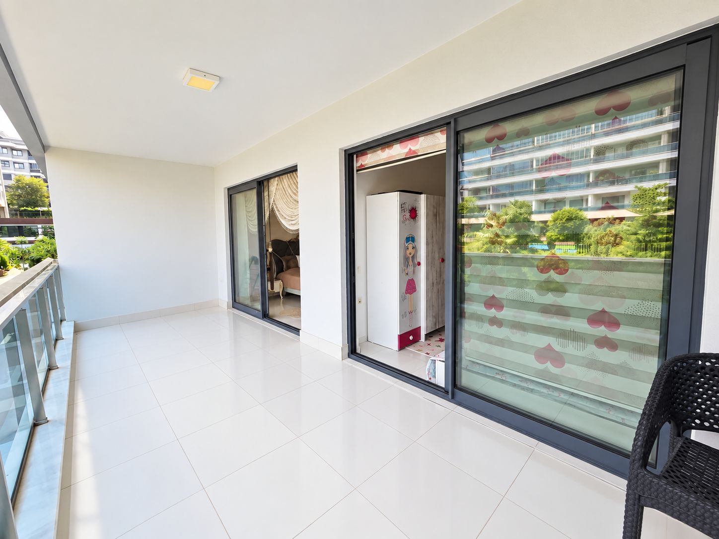 Long covered balcony with glass railing, wicker chair and views of landscaped grounds