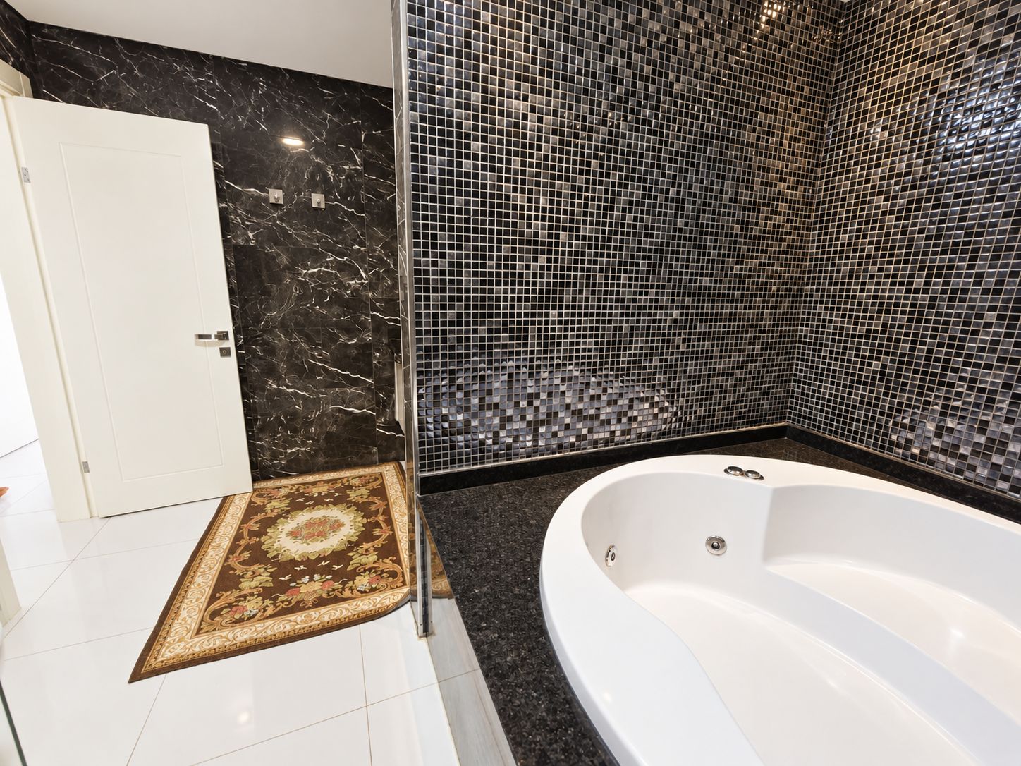 Bathroom with a round whirlpool tub, black mosaic walls and a glass partition in a duplex