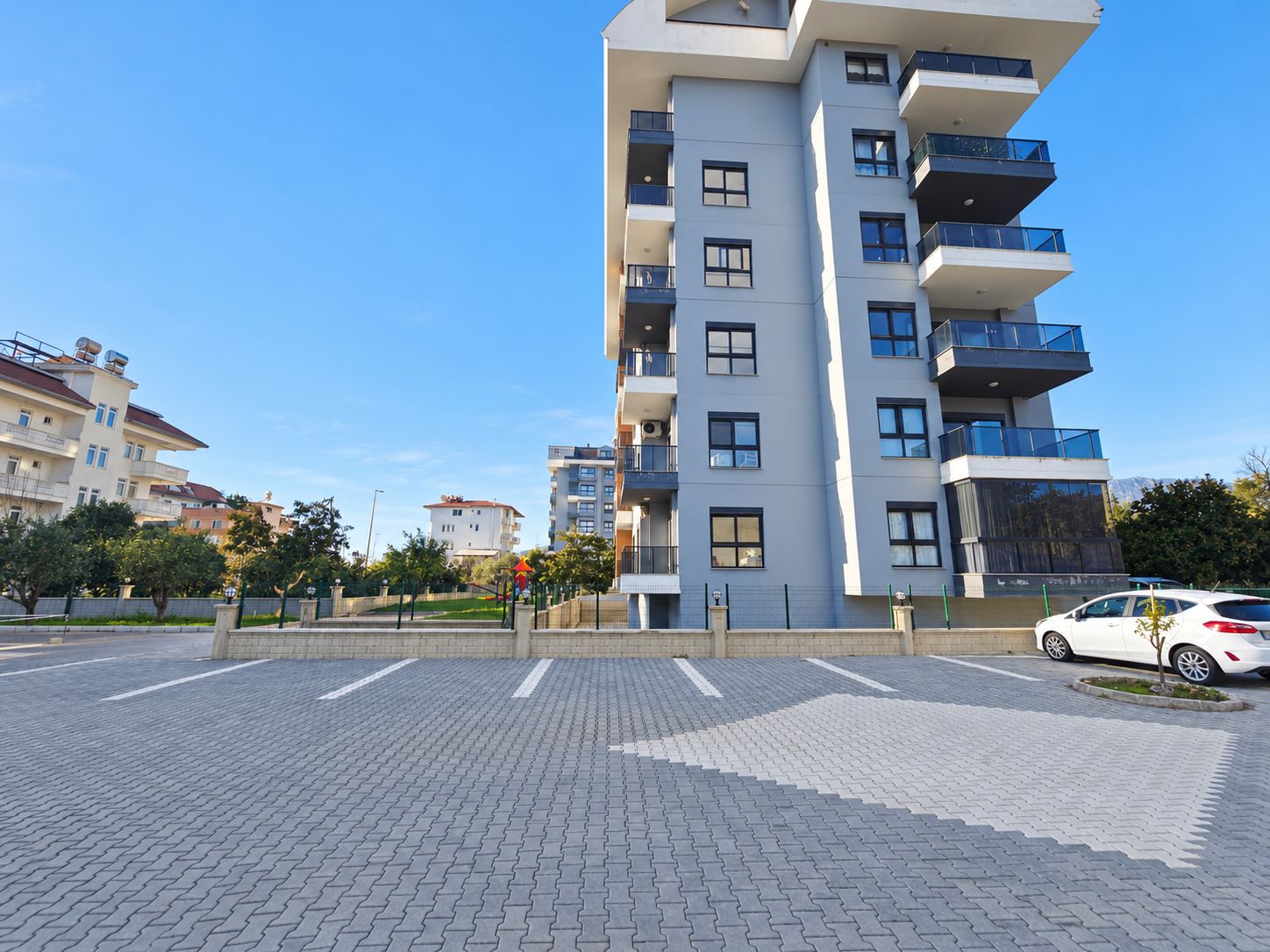 Beyaz çizgili taş döşeli otopark, Demirtaş'ta koyu cam balkonlu binanın yanında