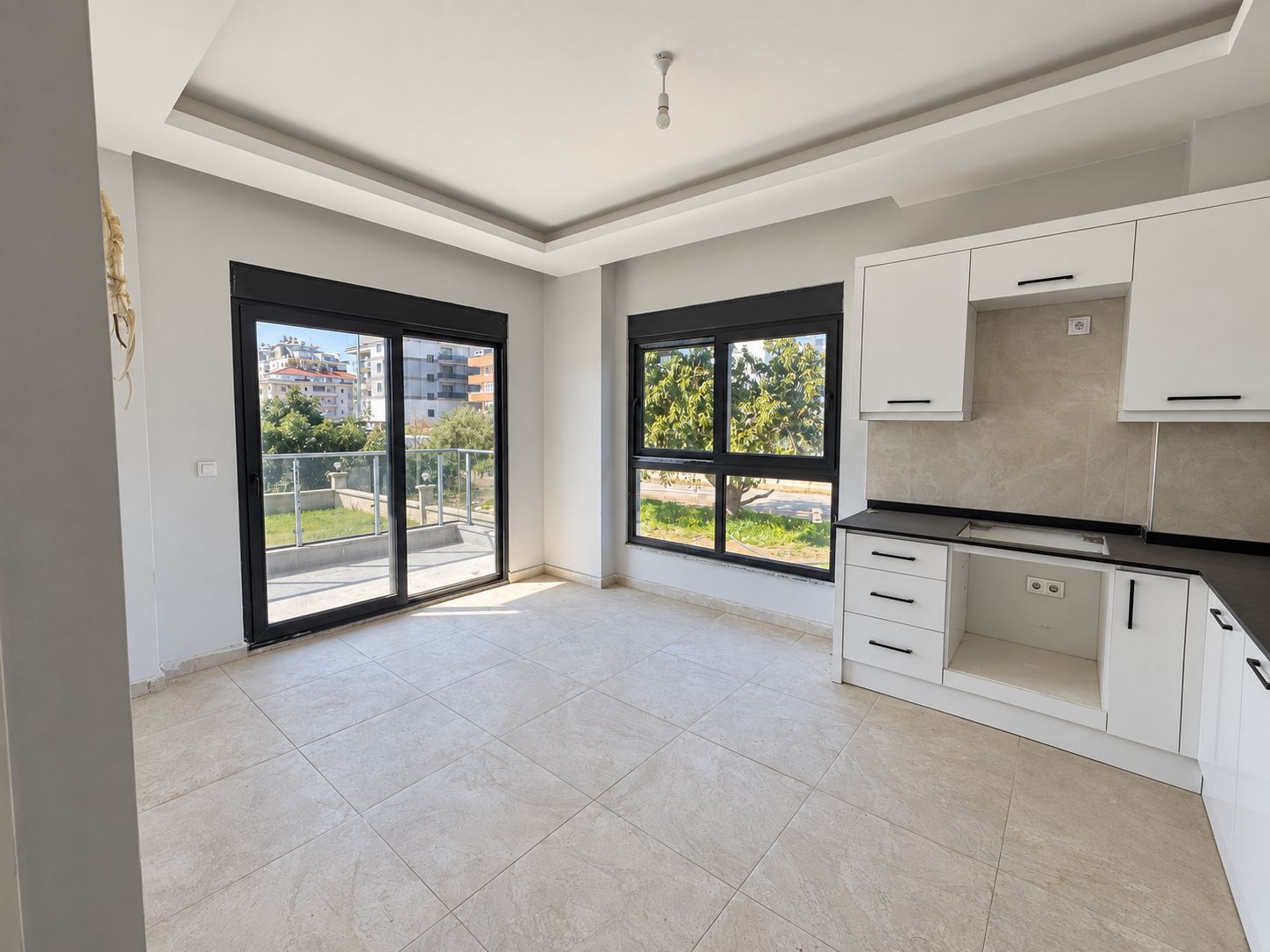 Kitchen-living room with white corner cabinetry and black countertop in a commercial unit in Demirtas