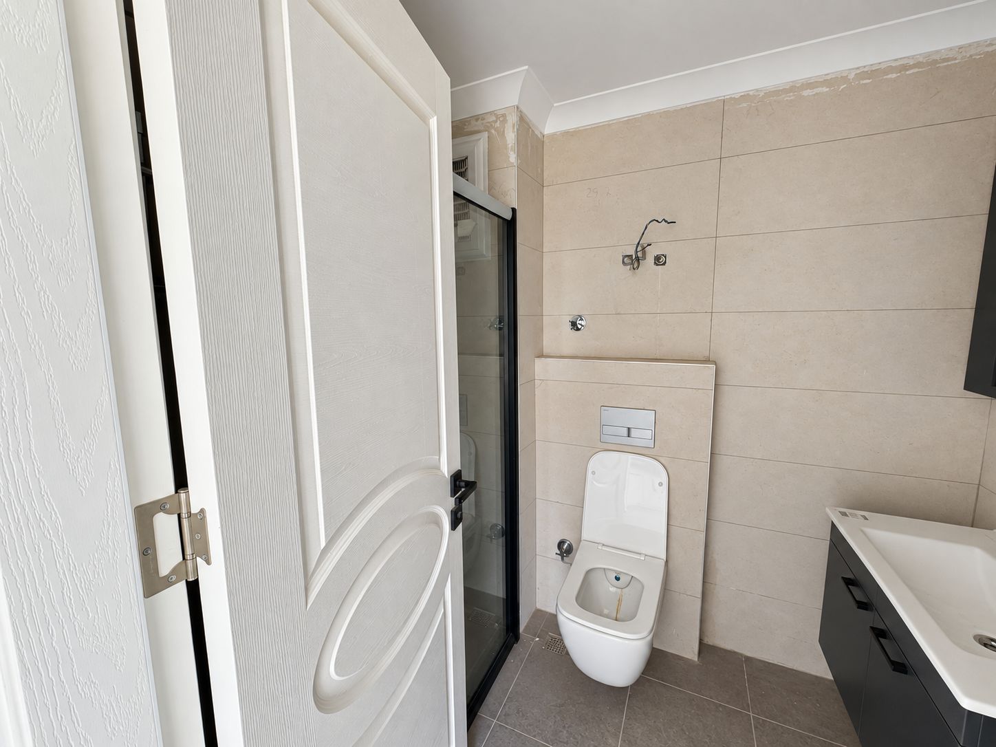 Bathroom with glass shower screen, wall-hung toilet and textured white door in Demirtas