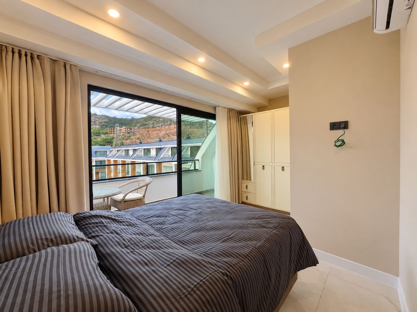 Yatak odasında deniz kenarında bulunan dublekse ait panoramik balkon kapısı ve gri çizgili örtü