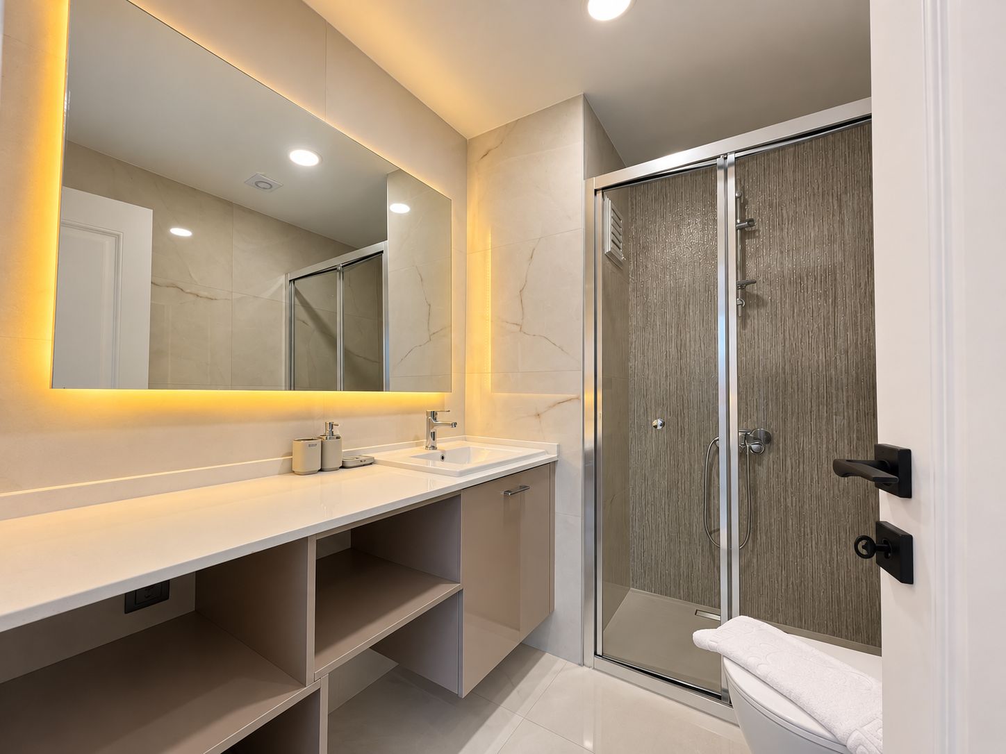 Banyoda rezidansa ait sürgülü cam duş kabini, uzun lavabo dolabı ve sıcak ışıklı ayna