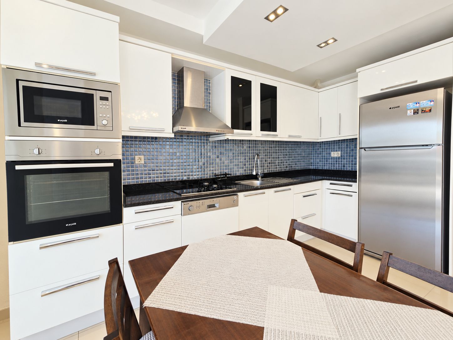 Kitchen with white corner cabinets, black stone countertop and blue mosaic backsplash in Konakli