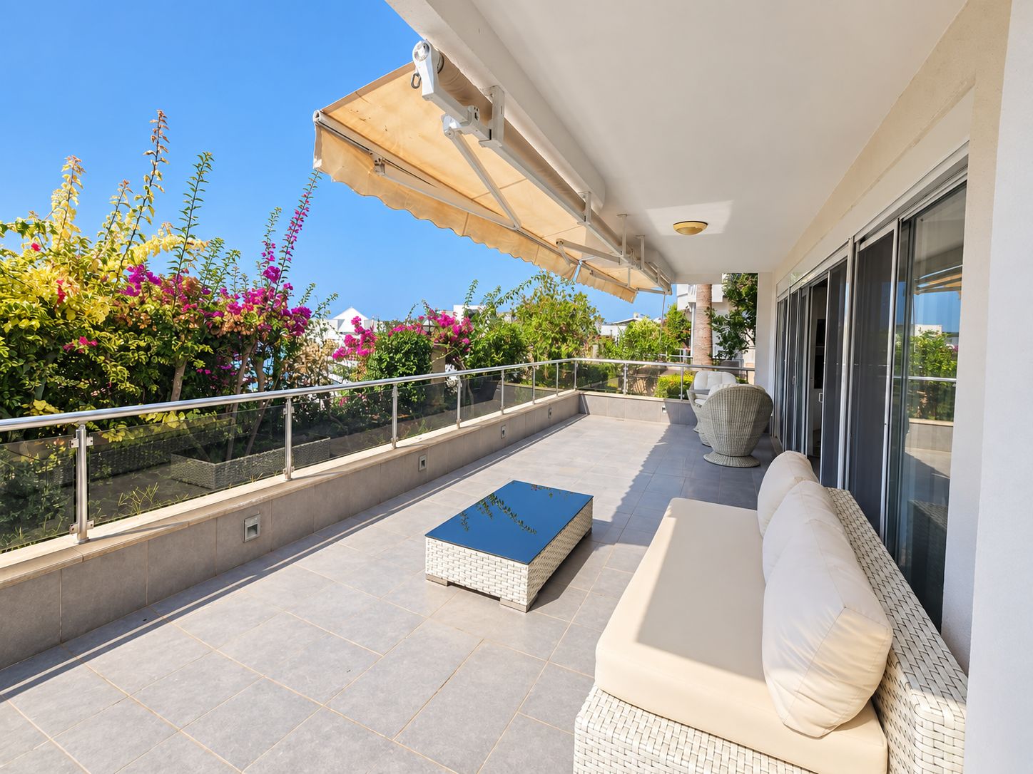 Spacious terrace with wicker sofa, glass railing and flowering shrubs at a 2+1 apartment for sale in Turkey