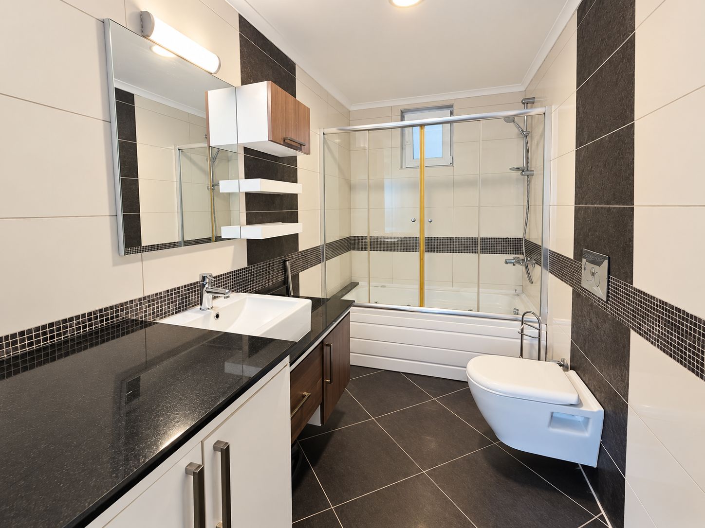Bathroom with a bathtub shower, long black countertop and illuminated mirror in a flat in Konakli