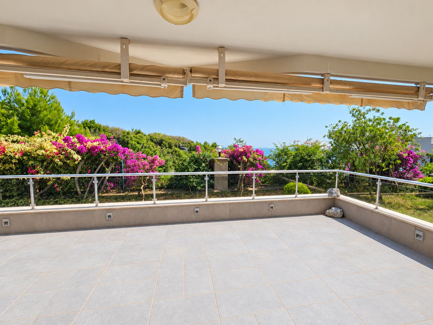 Open terrace with bougainvillea, glass railing and sea view at a home for sale