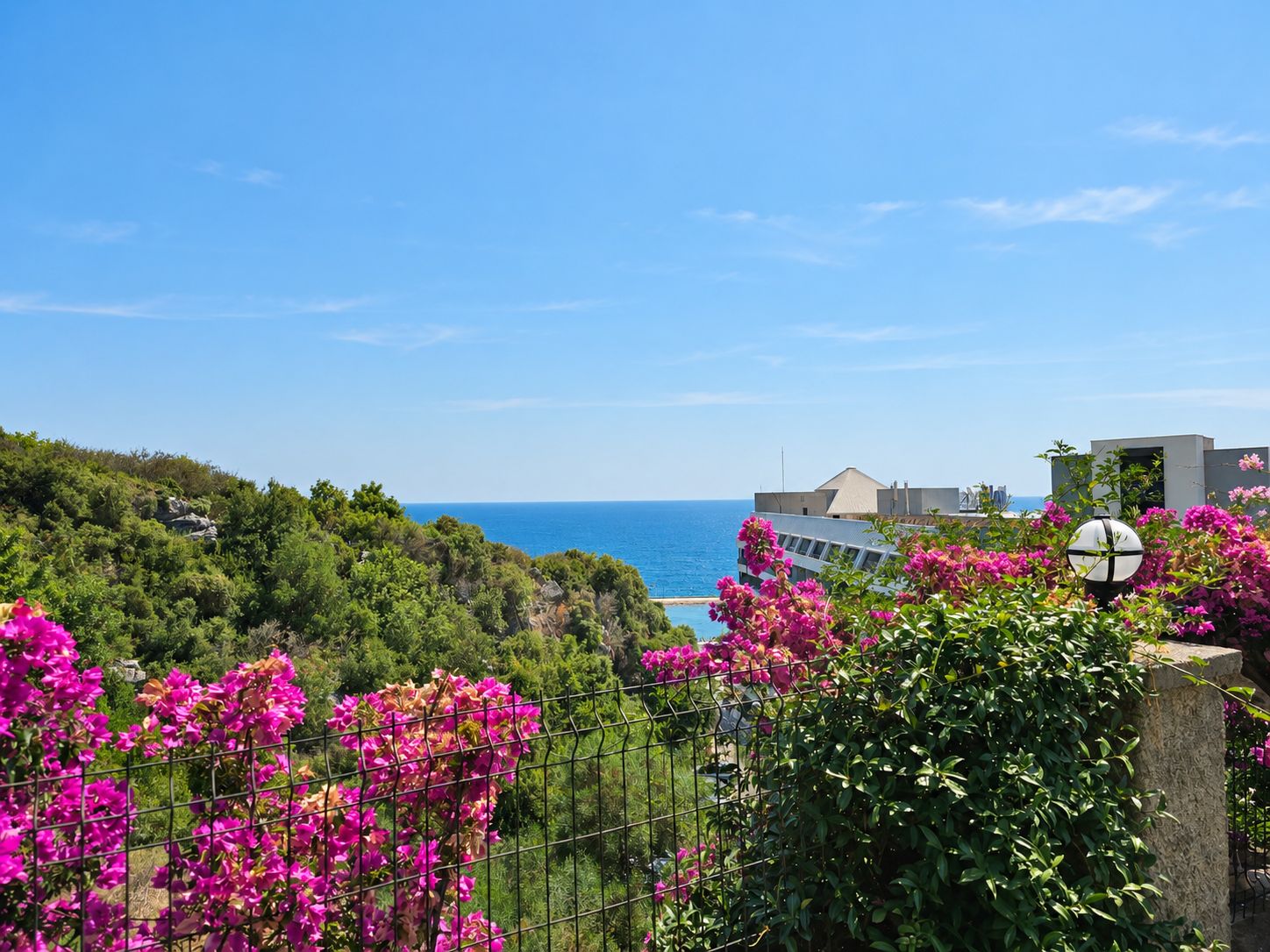 Blue sea view over a green hillside and pink flowering shrubs from apartments in Konakli