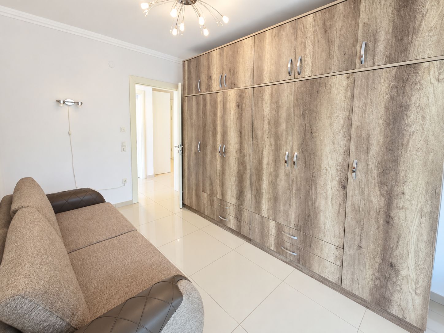 Living room with a wall-length built-in wardrobe and gray-brown sofa in a 2+1 home in Turkey