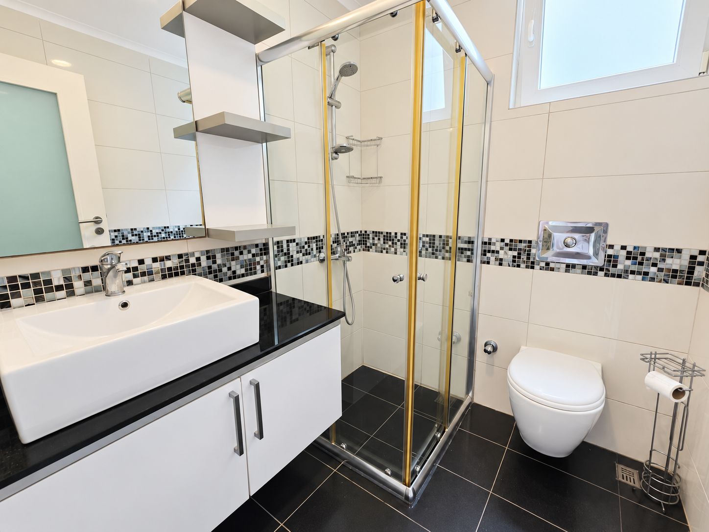 Bathroom with glass shower enclosure, black countertop and mosaic border in a residence in Konakli