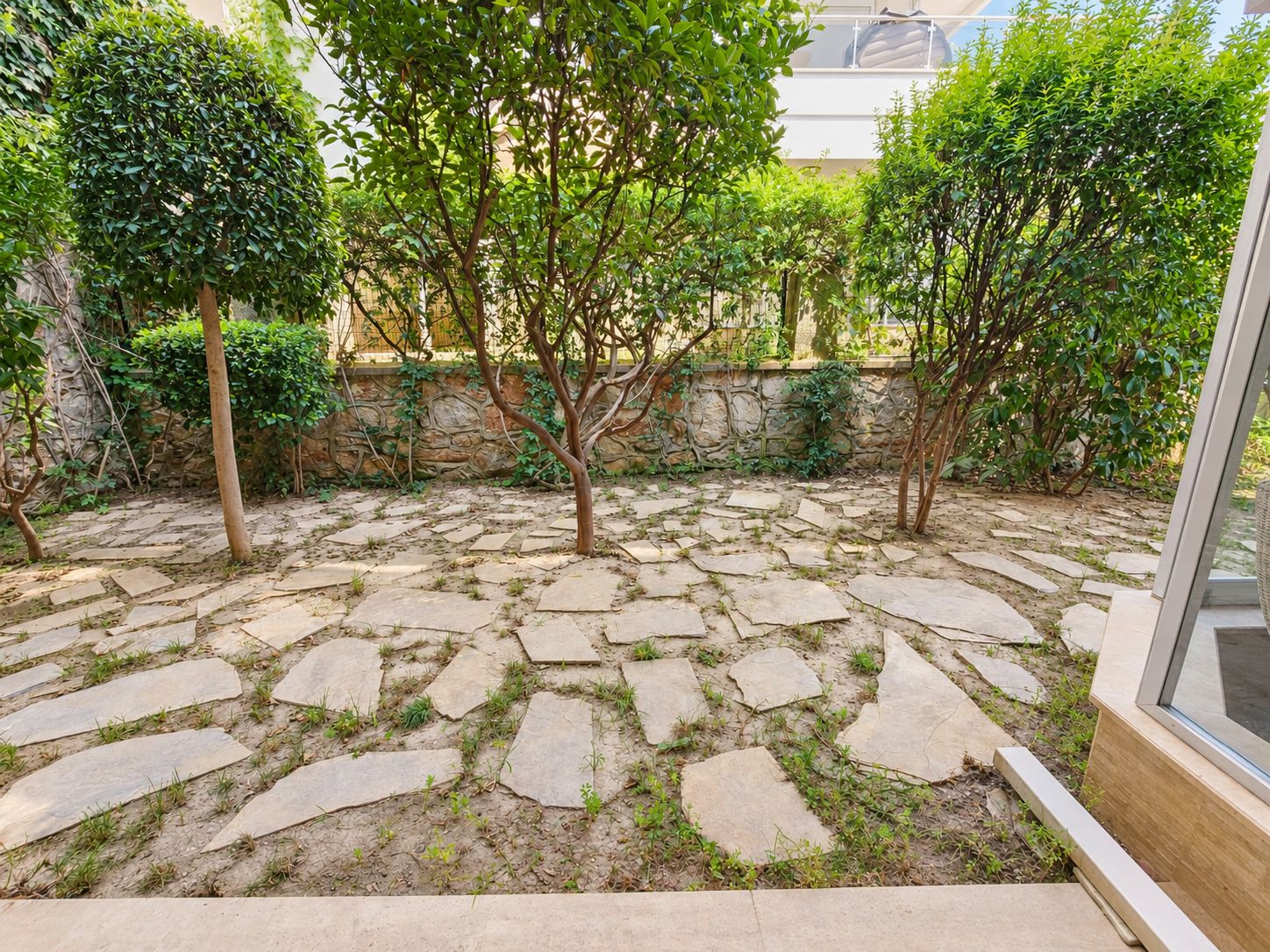 Small garden with fruit trees, stone paving and a glazed terrace beside an apartment